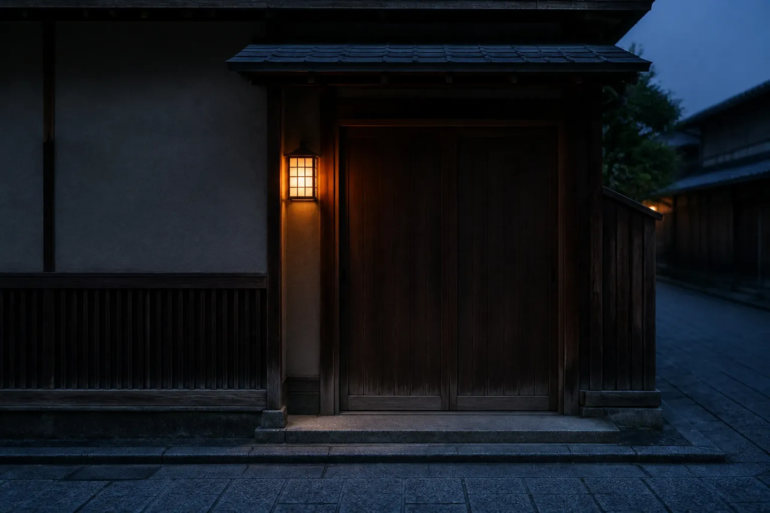 An unmarked wooden sliding door of a Kyoto ochaya teahouse in the Gion district, closed at dusk with a single paper lantern glowing beside it, no signage visible