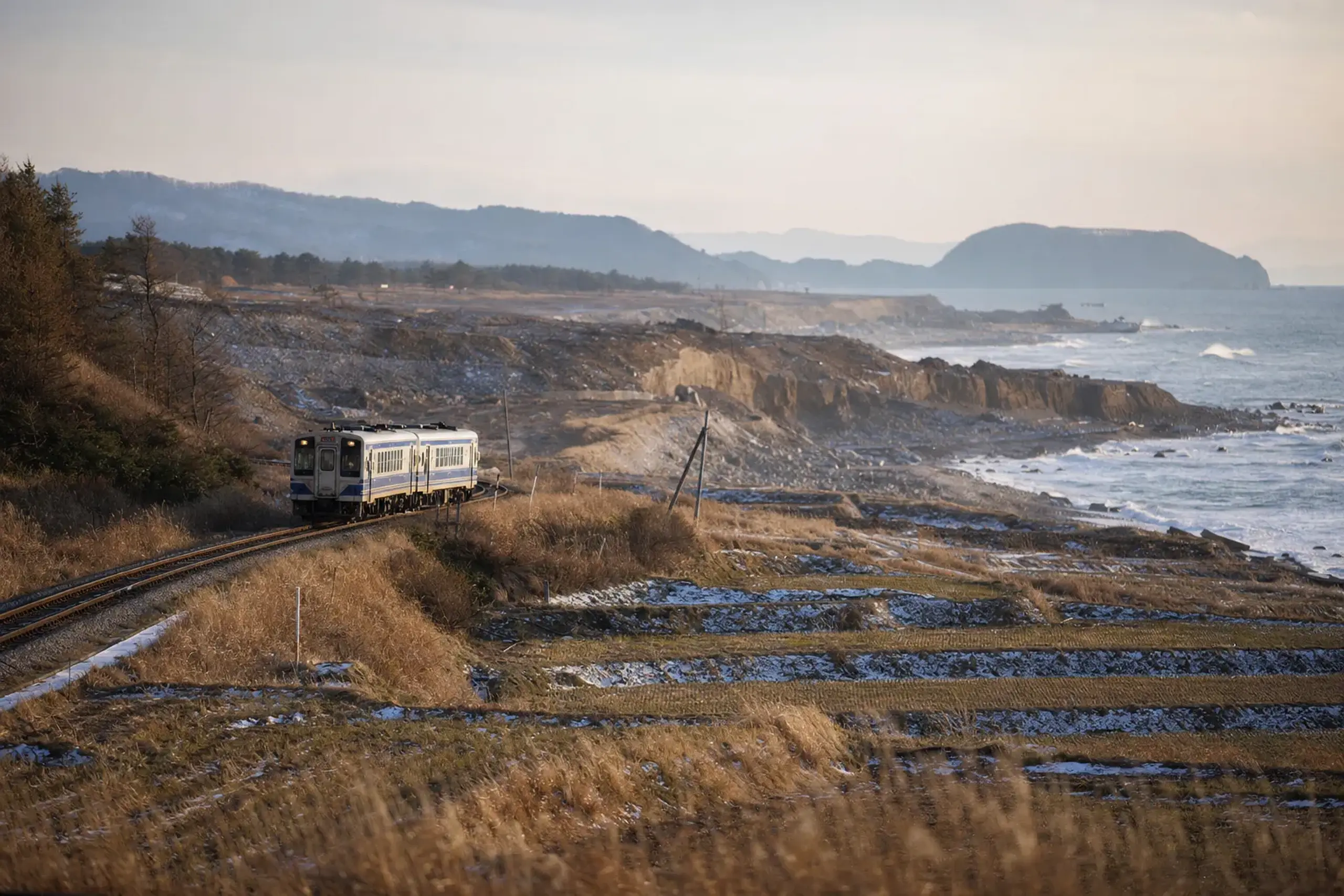 A Noto Railway train running along the restored full line, tracks curving past coastal countryside on the Noto Peninsula