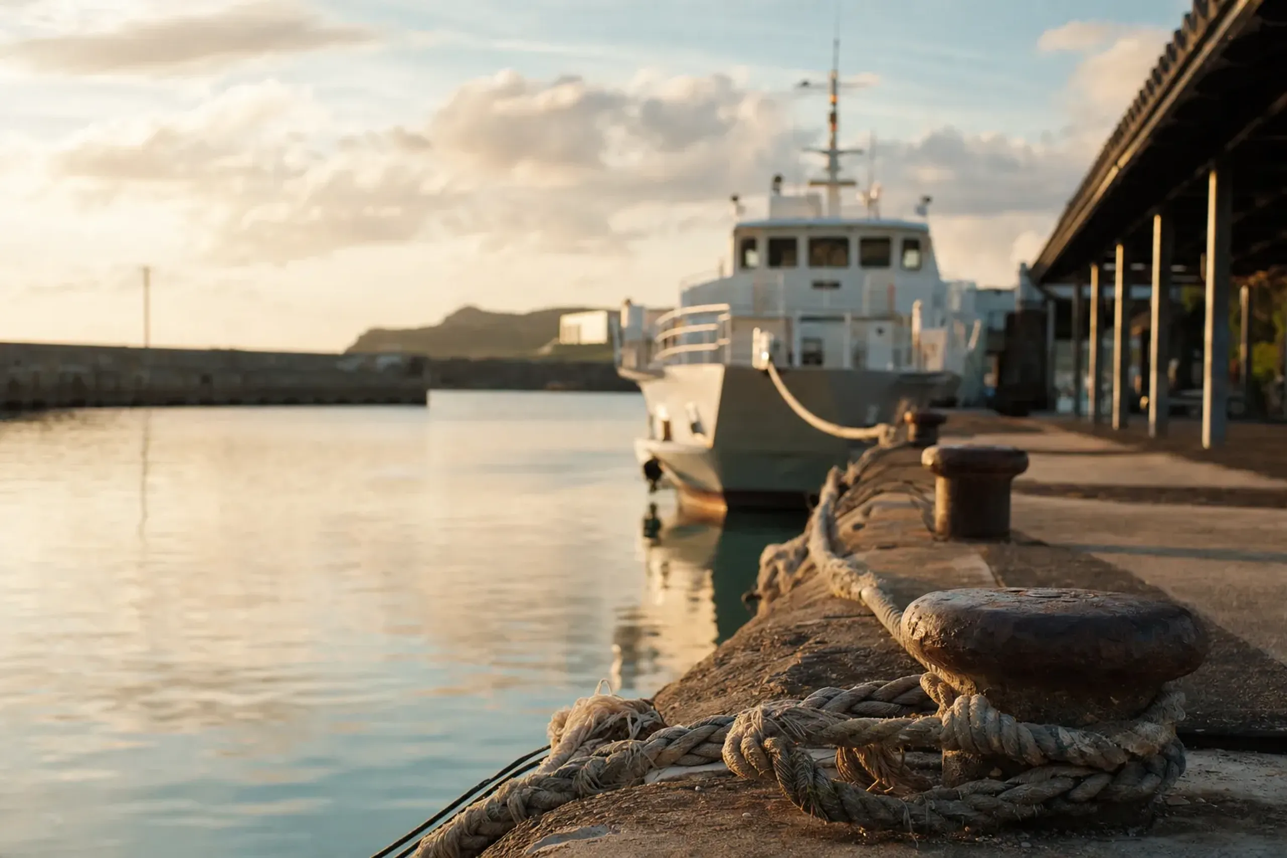 a small inter-island ferry moored at an Okinawan harbor pier with tie ropes and bollards in the foreground