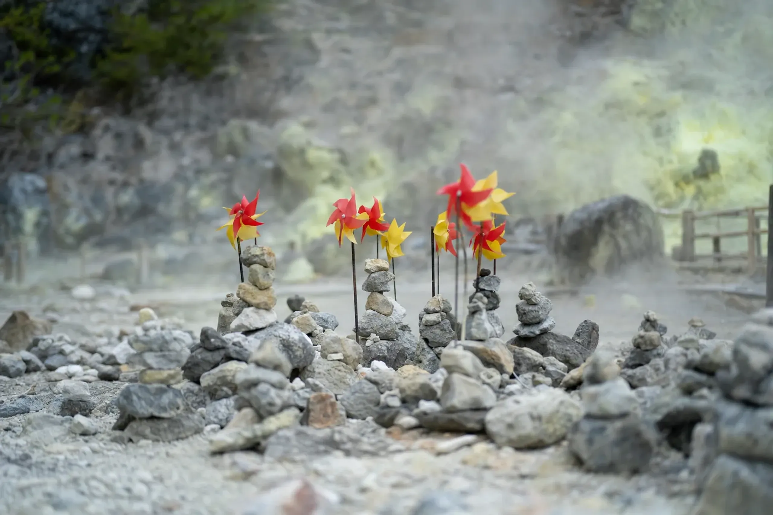 A quiet stony stretch of Sai-no-Kawara at Osorezan with hand-stacked stone cairns and bright plastic pinwheels turning in the sulfurous air