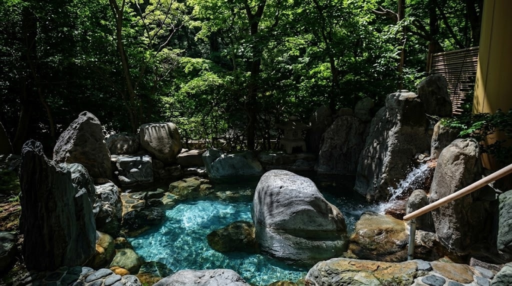 A tranquil open-air hot spring bath surrounded by natural stone and vibrant green trees.