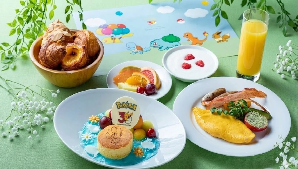 Pokémon-themed breakfast spread with pastries, fruit plate, yogurt with raspberries, orange juice, and an omelette plate on a light green table.