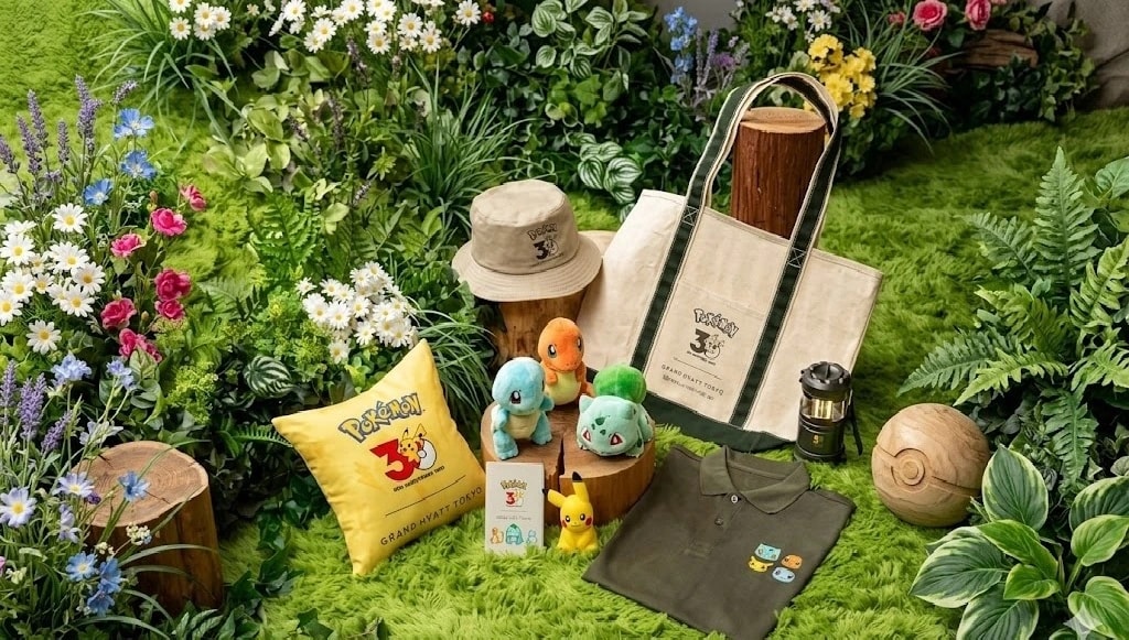 Display of Pokémon 30th anniversary merchandise in a garden scene: tote bag, plush Pokemon, hat, yellow pillow, polo shirt, and card set amid flowers and greenery.
