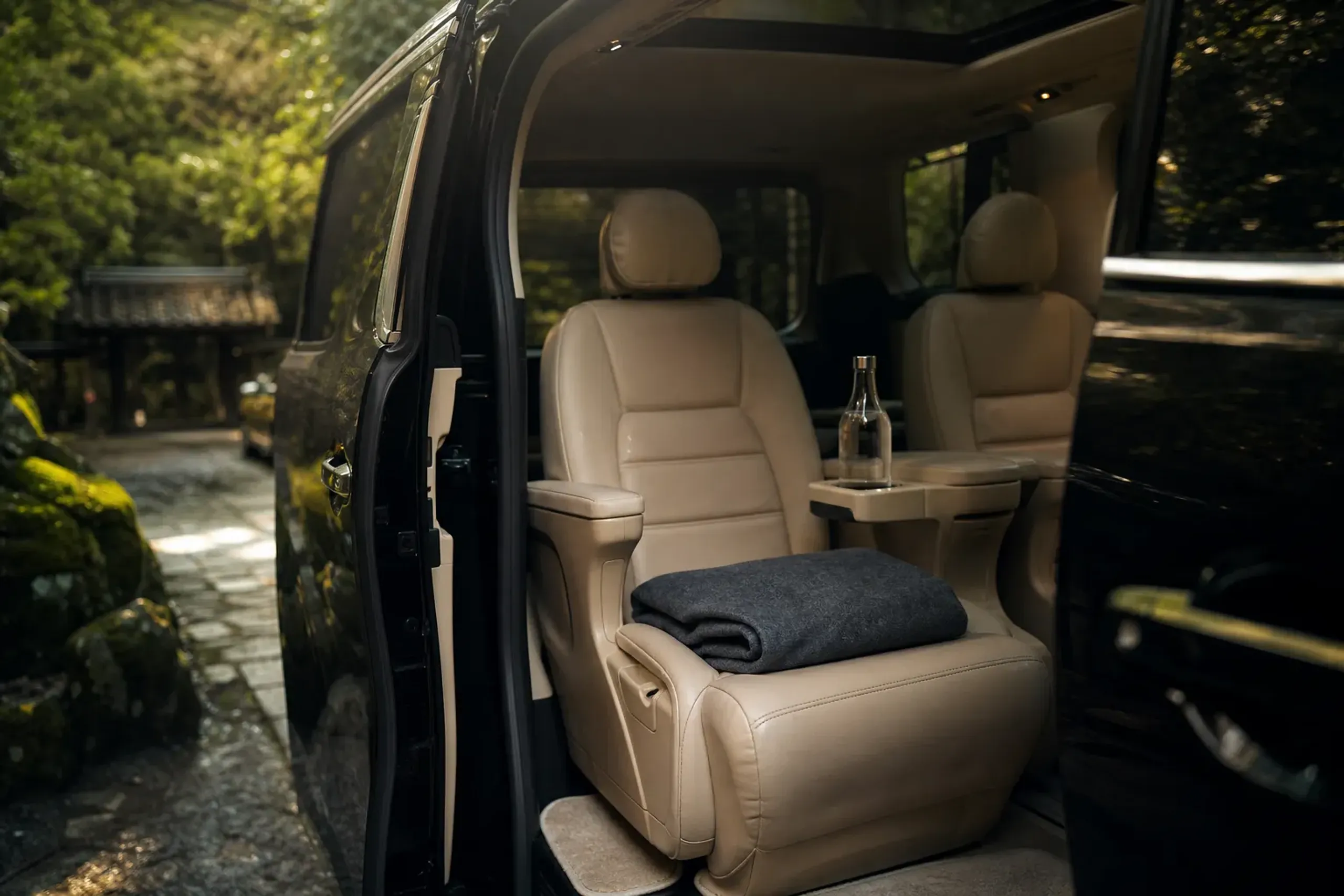 The immaculate leather rear passenger cabin of a Toyota Alphard with folded blankets and a bottle of water, empty and ready