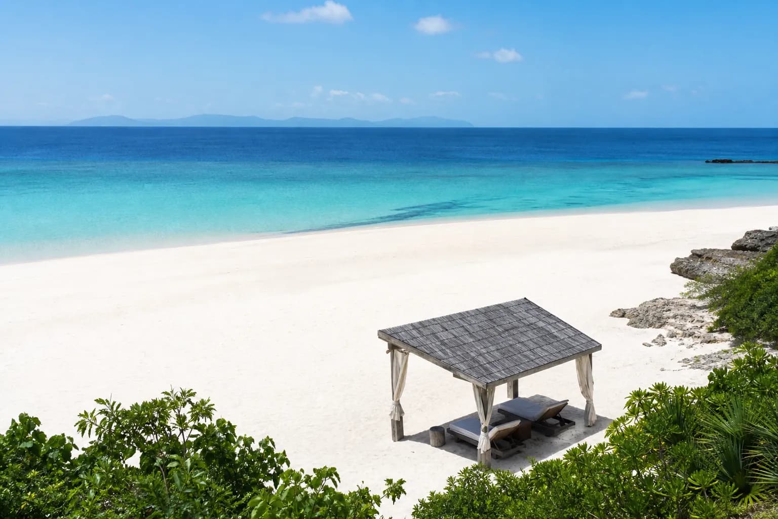 Quiet Okinawa resort beach with a private cabana and empty loungers by turquoise water