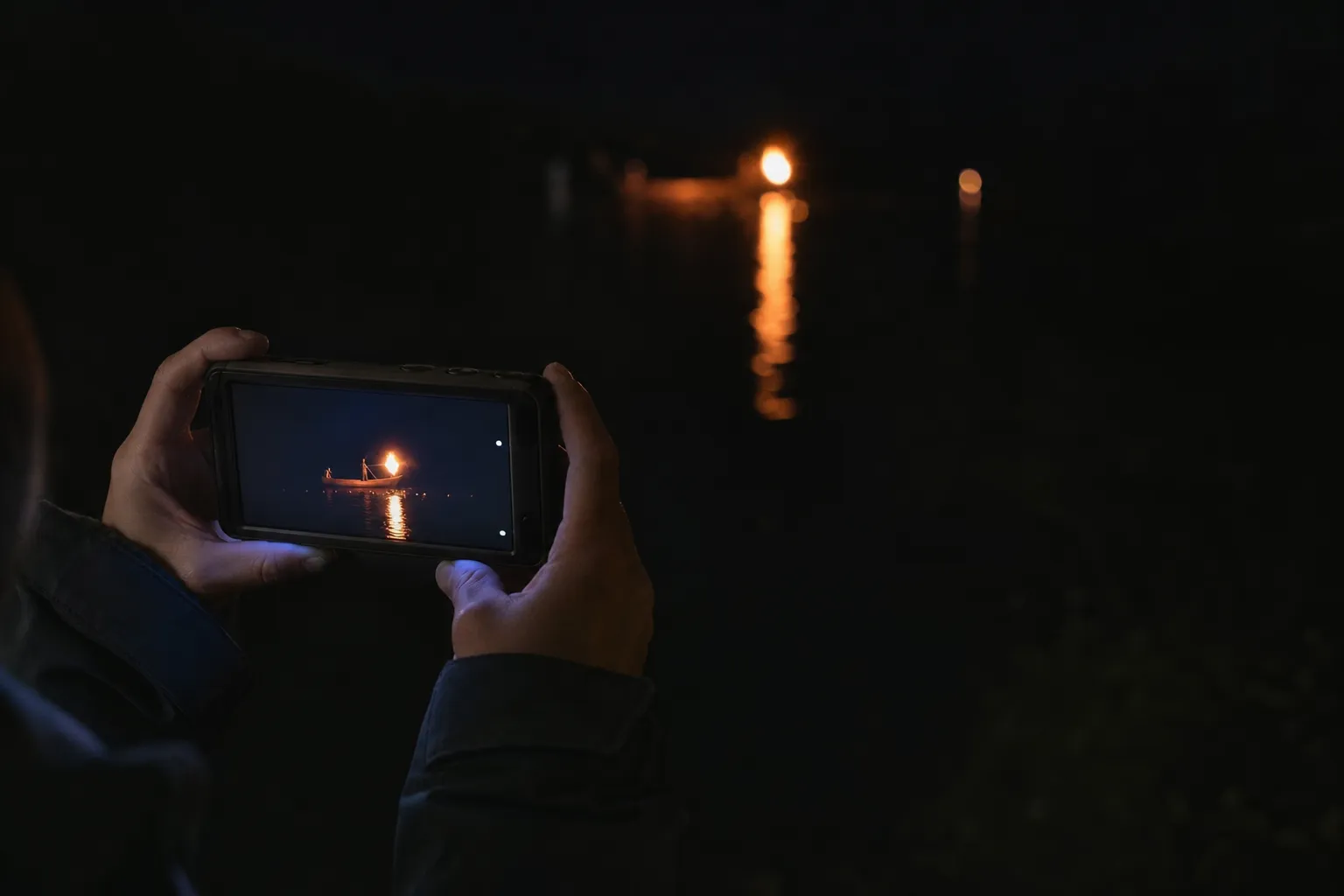 Low-light photo of a camera capturing torchlight on a river without flash during ukai