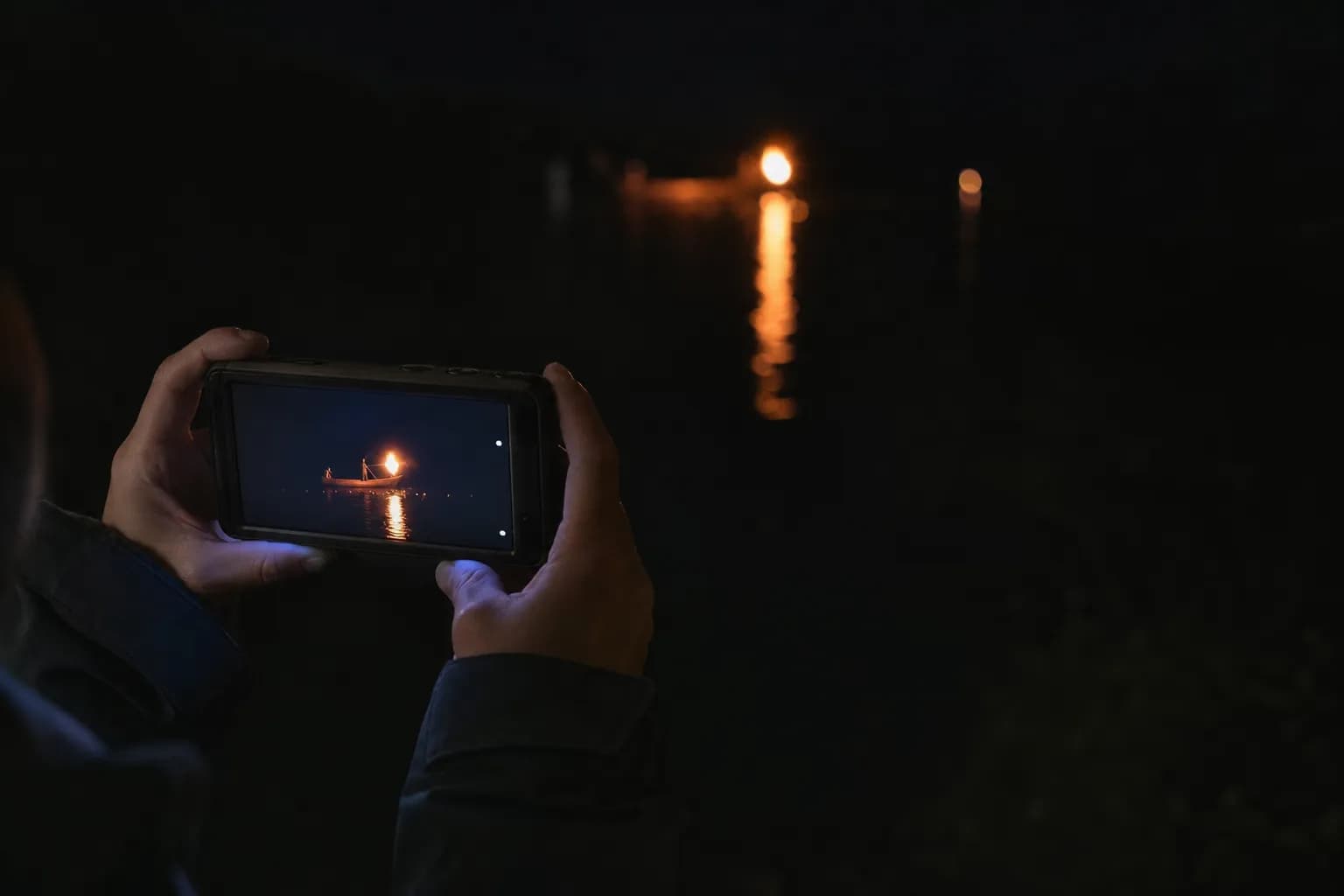 Low-light photo of a camera capturing torchlight on a river without flash during ukai
