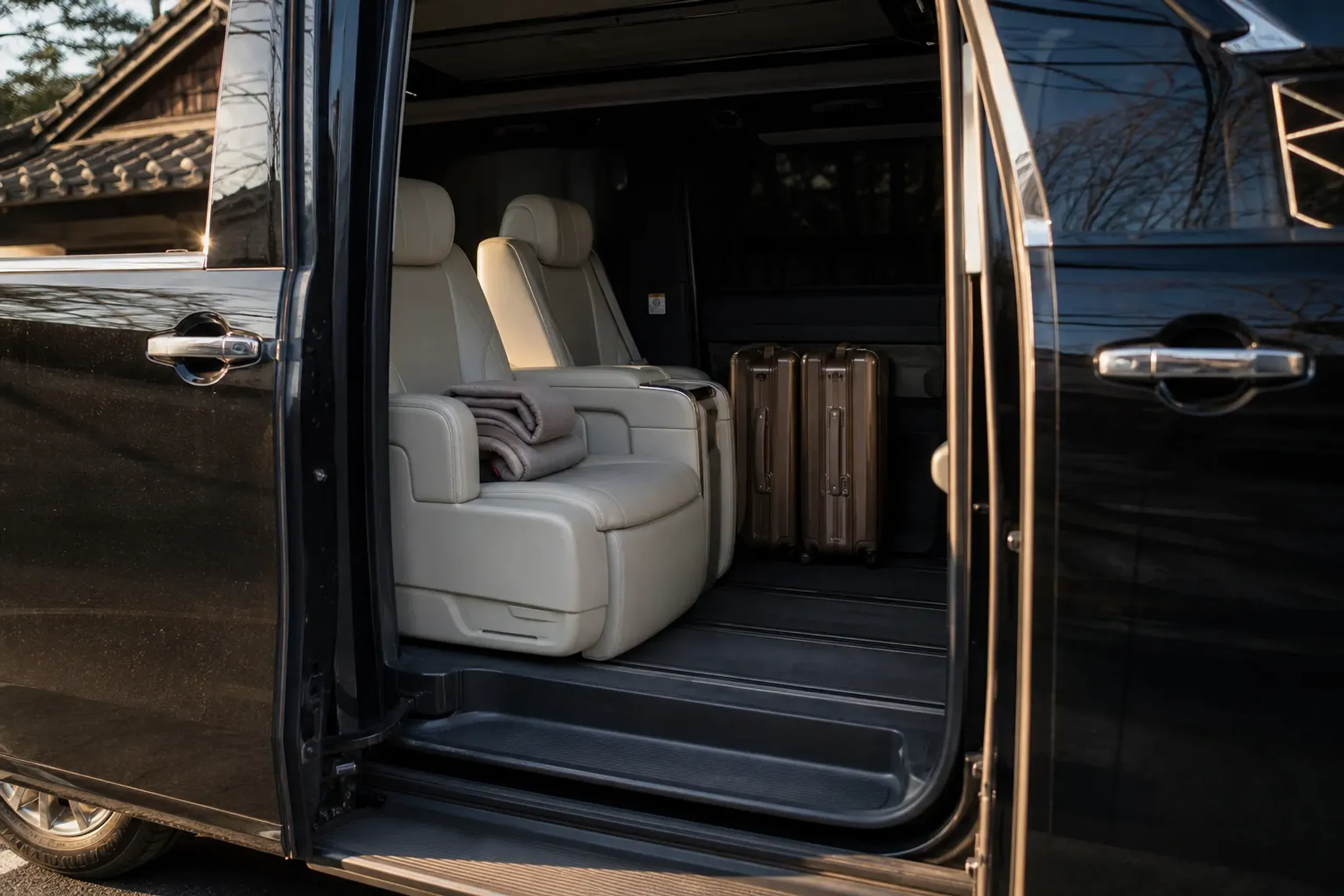The quiet captain-seat interior of a Toyota Alphard with two suitcases stowed, viewed through the open sliding door