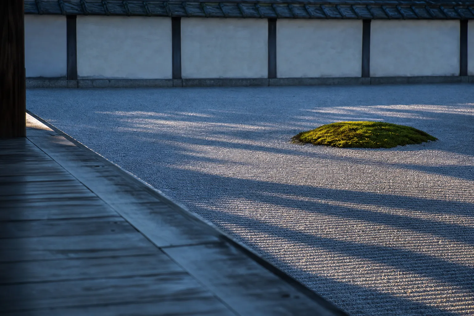 A serene Kyoto temple garden of raked gravel and moss at first light, with long dawn shadows and no visitors, viewed along the edge of a wooden temple veranda