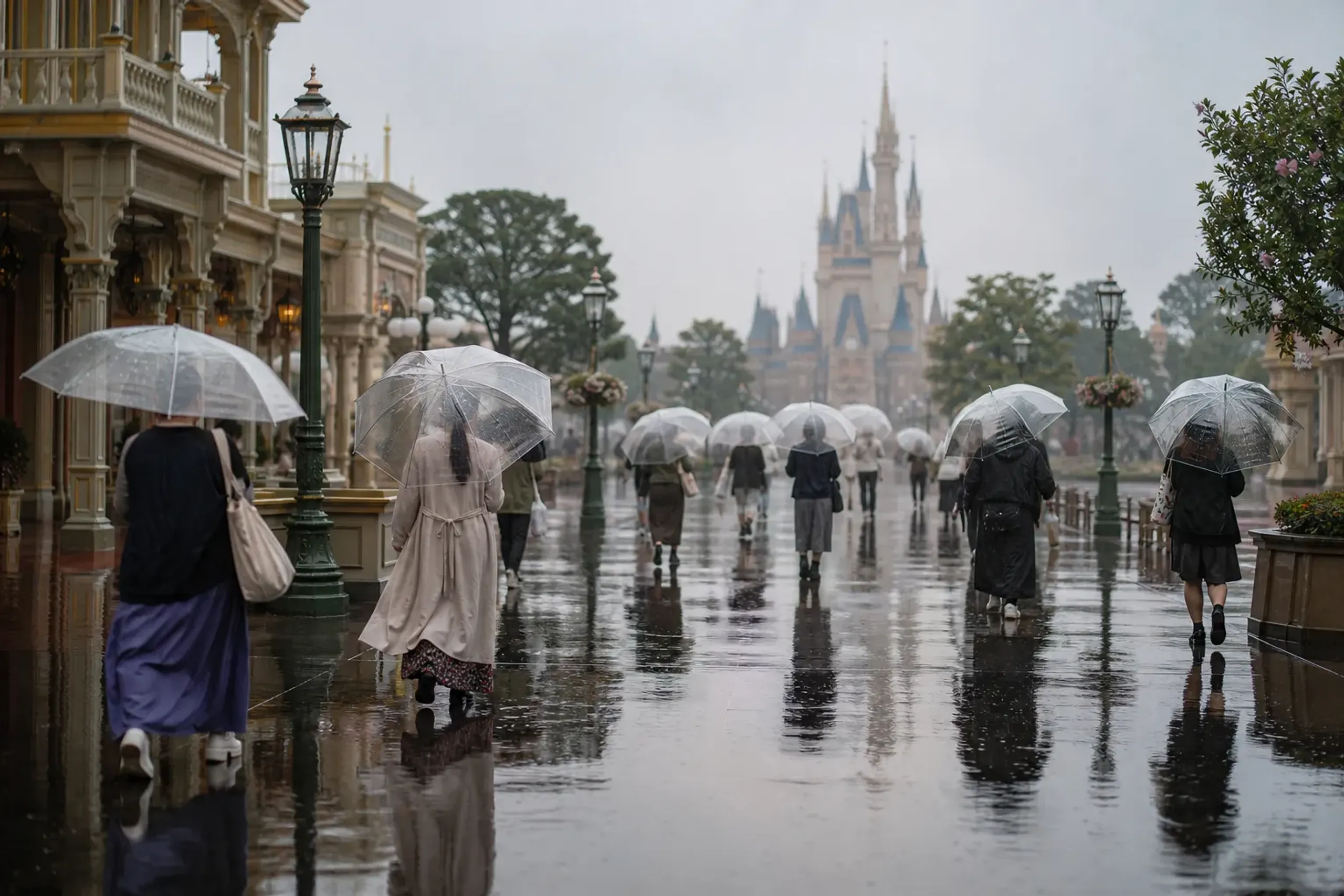 Guests with clear umbrellas on a wet walkway near a Tokyo theme park during rain