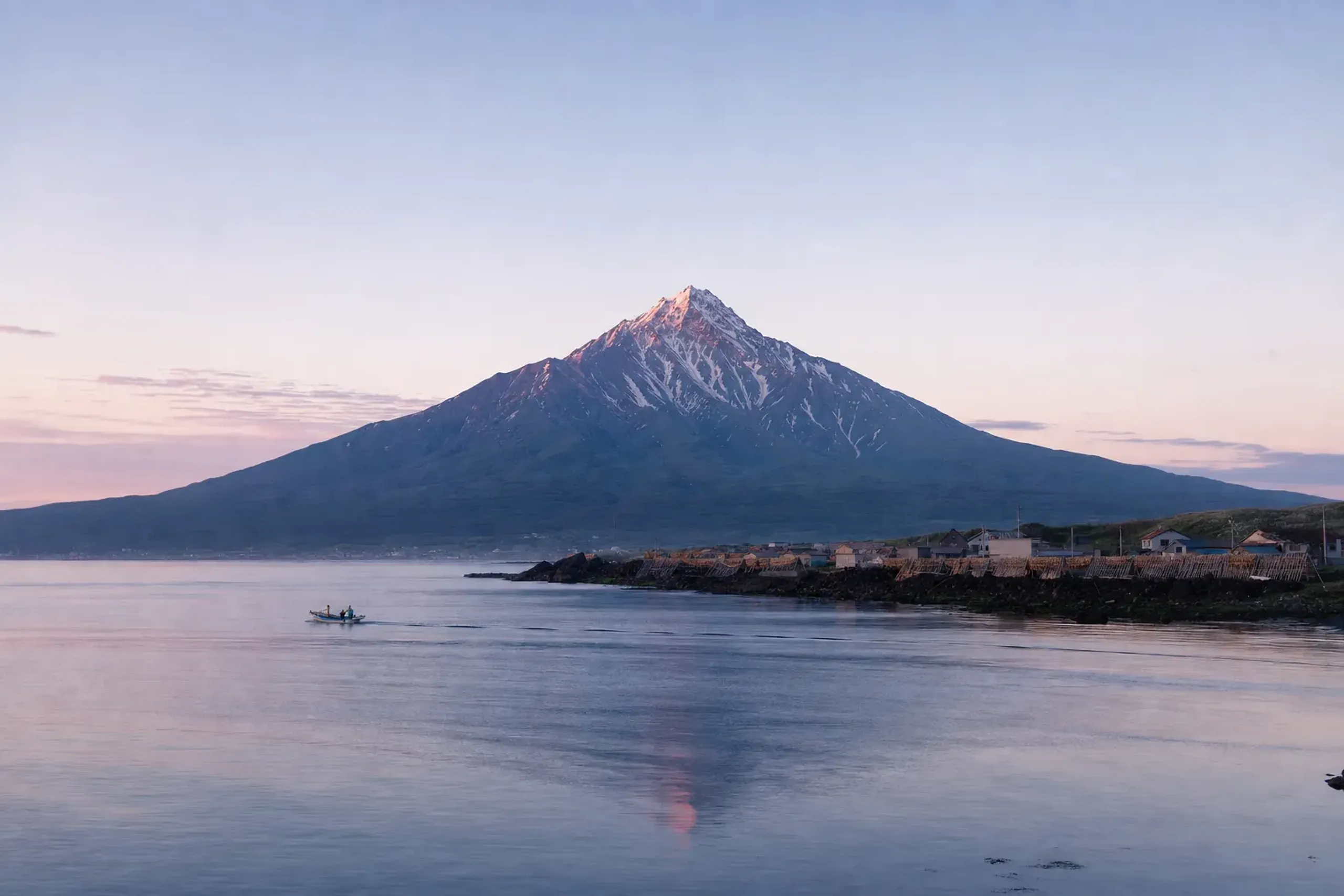 The symmetrical volcanic cone of Rishiri-Fuji rising directly from the ocean, with kombu-harvesting communities hugging the rocky coastal perimeter at its base