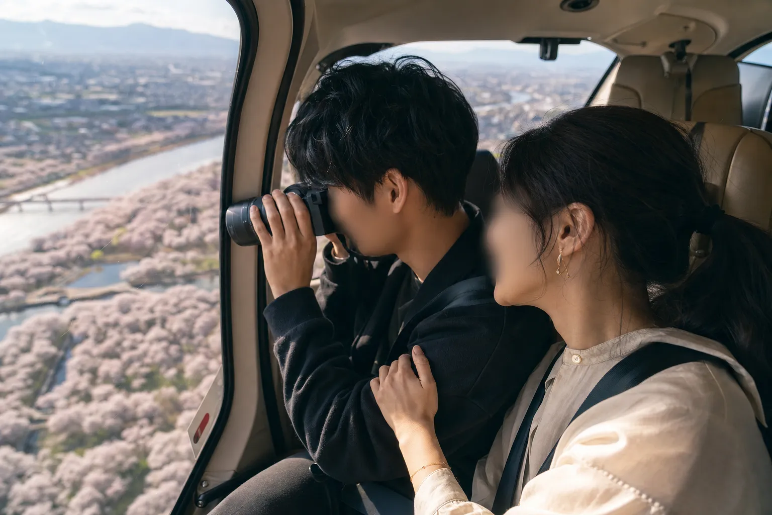 A couple smiling and taking a photograph out the window of a helicopter during a clear spring day.