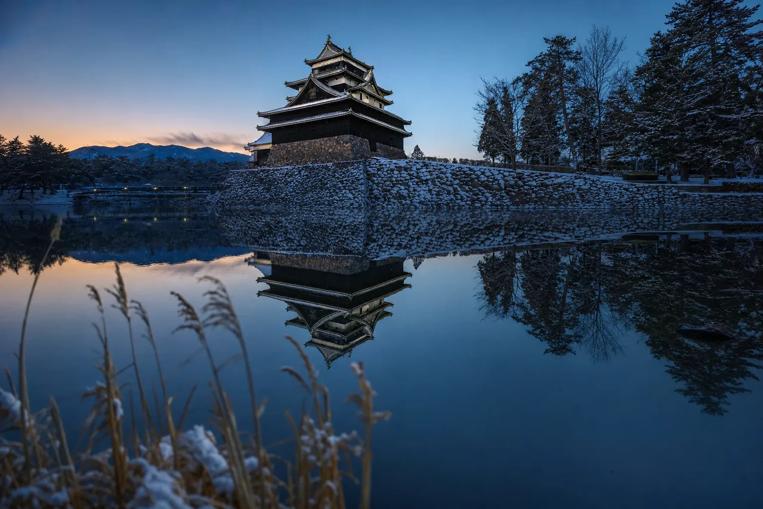 the original wooden keep of Matsue Castle rising above its moat, reflected in the still waters of Lake Shinji at dusk
