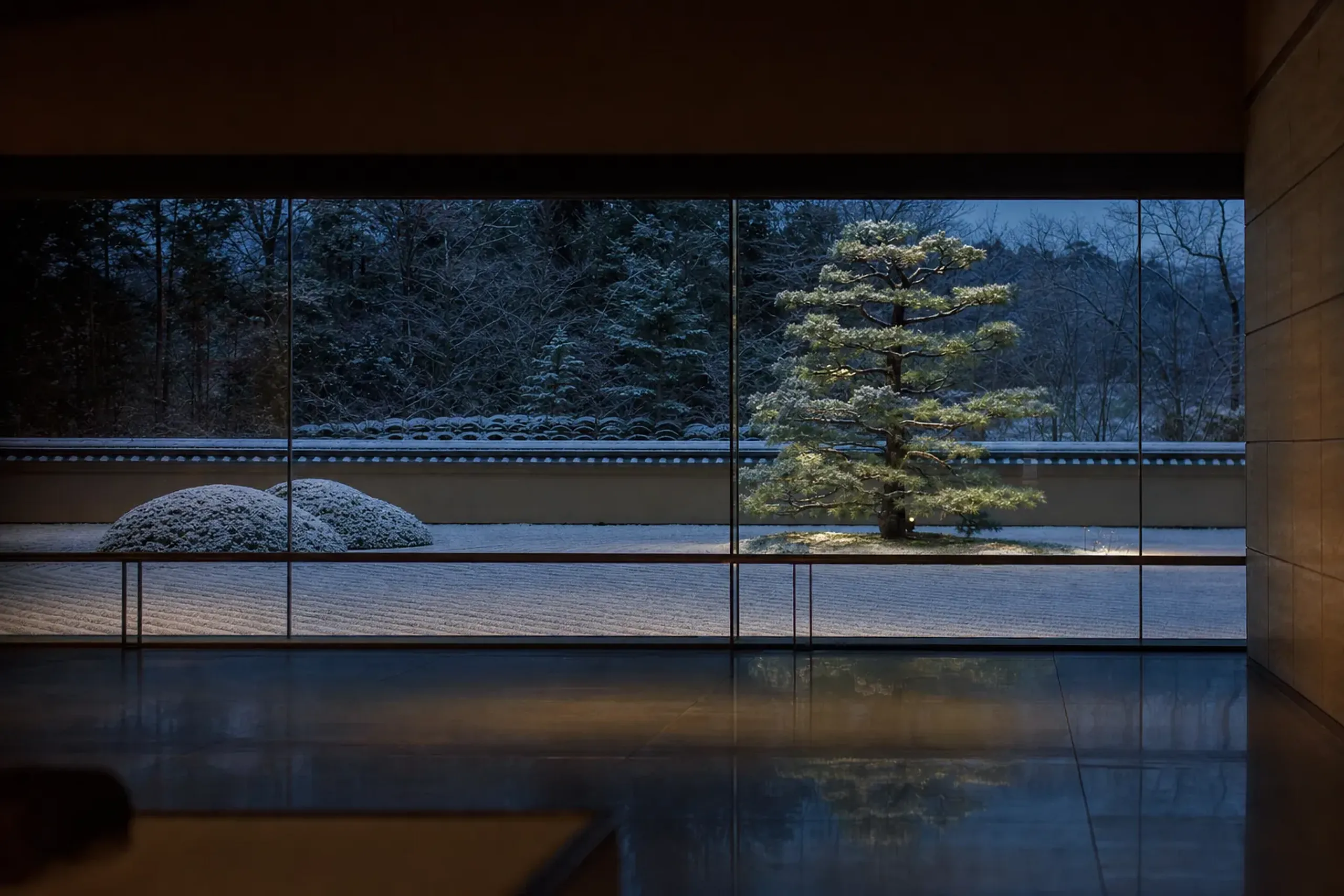 the meticulously raked white gravel, moss mounds, and pruned pines of the Adachi Museum garden framed through a vast plate-glass gallery window