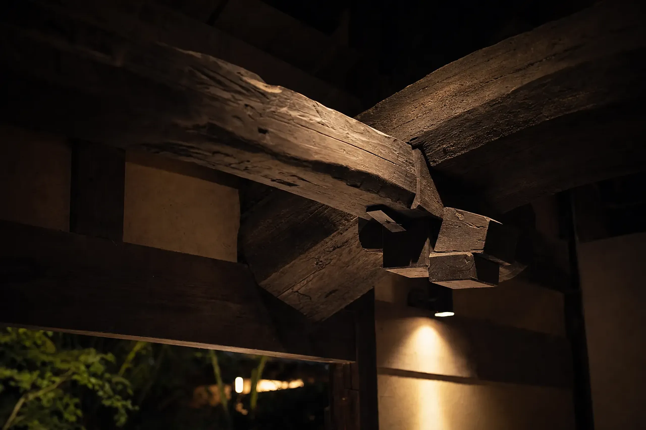 aged dark timber ceiling beams and exposed wood grain frames of a relocated traditional minka at Sanso Murata, Yufuin, lit by deliberate low lamplight