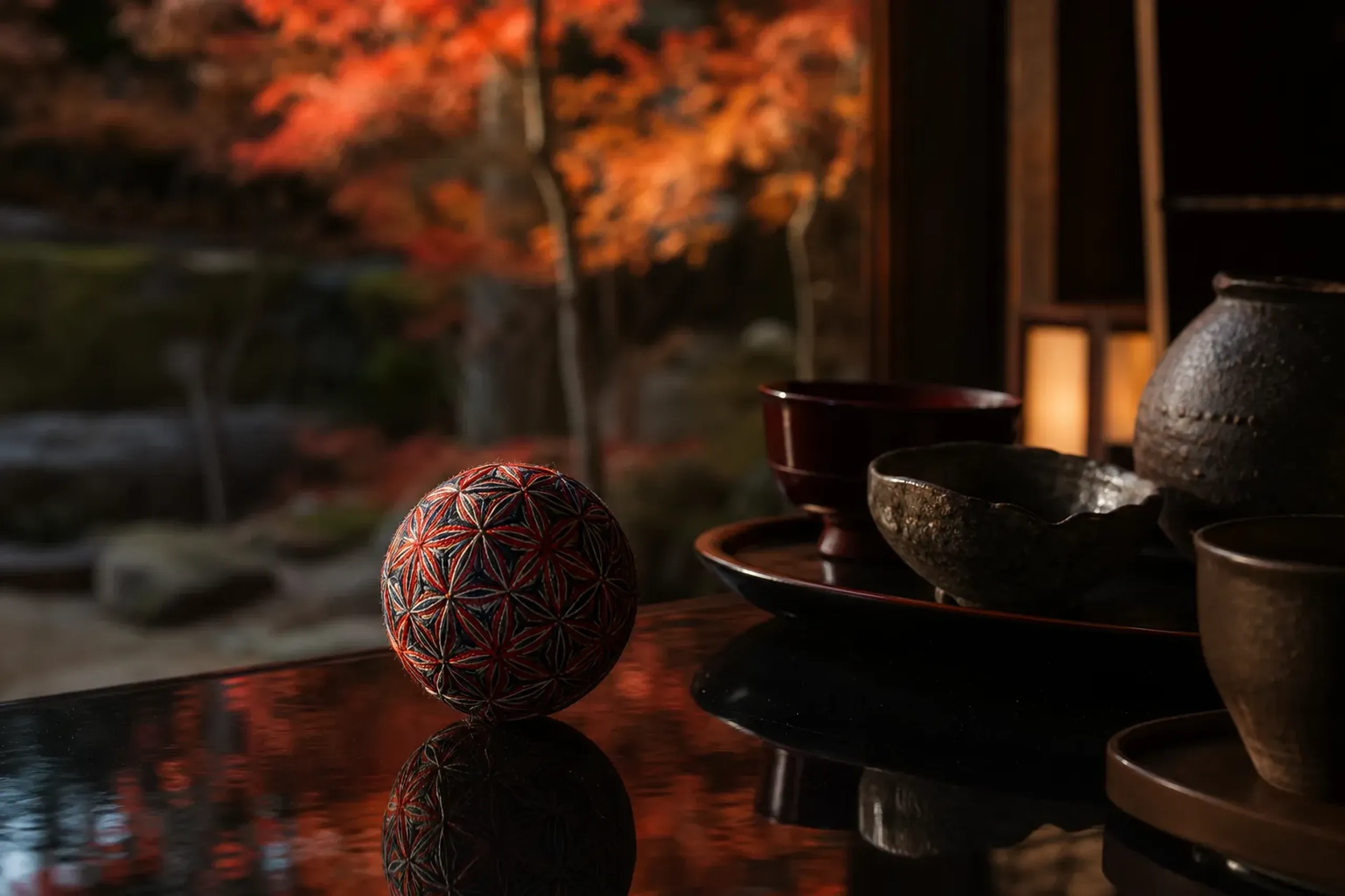 a single completed asanoha-patterned Sanuki temari resting alone on a lacquer surface, contrasted against lacquerware, stone and ceramic craft objects set aside in the background