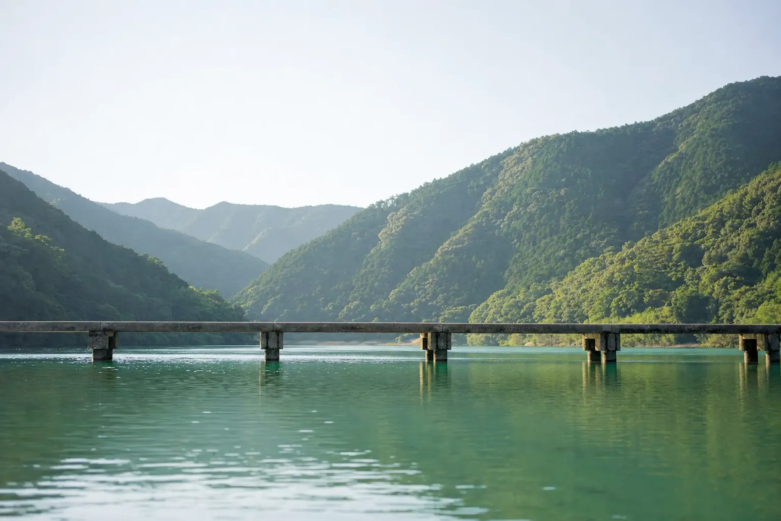 A pale chinkabashi sinking bridge crossing the width of the Shimanto River, its low railless deck sitting just above the flowing water