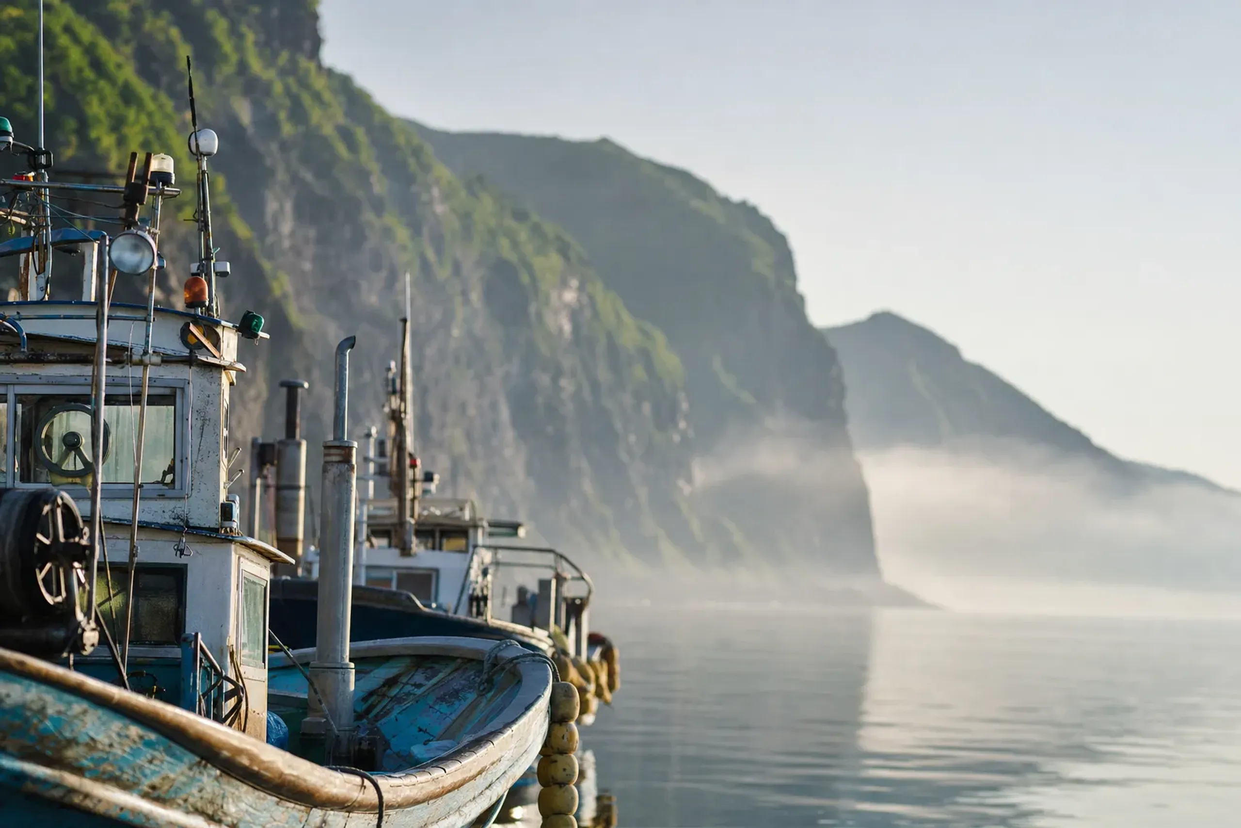 the fishing harbor town of Utoro on the Sea of Okhotsk coast, weathered boats moored below coastal cliffs at the base of the Shiretoko Peninsula