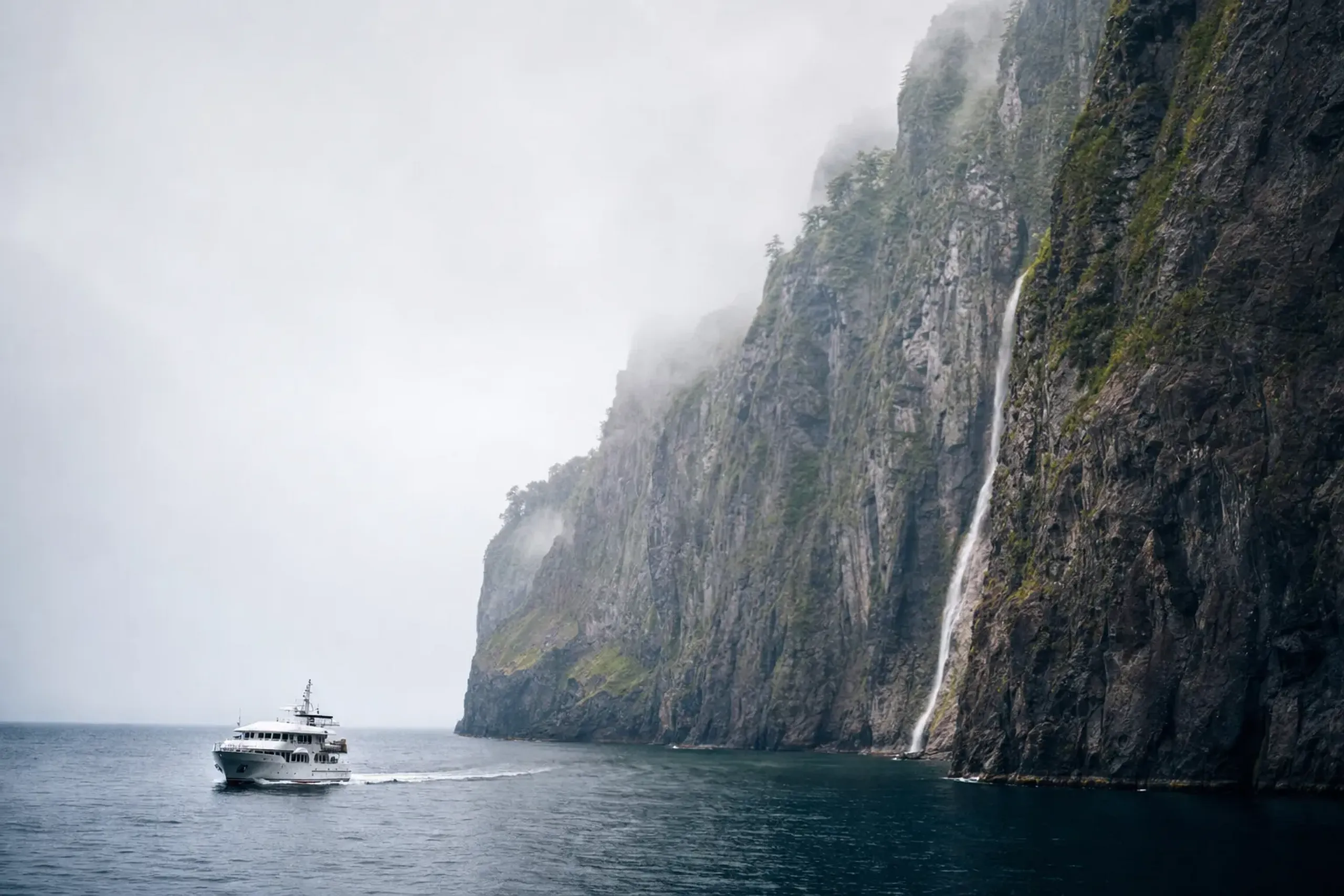 a sightseeing cruise boat cutting across the Sea of Okhotsk beneath the sheer sea cliffs and waterfalls of the Shiretoko Peninsula coastline