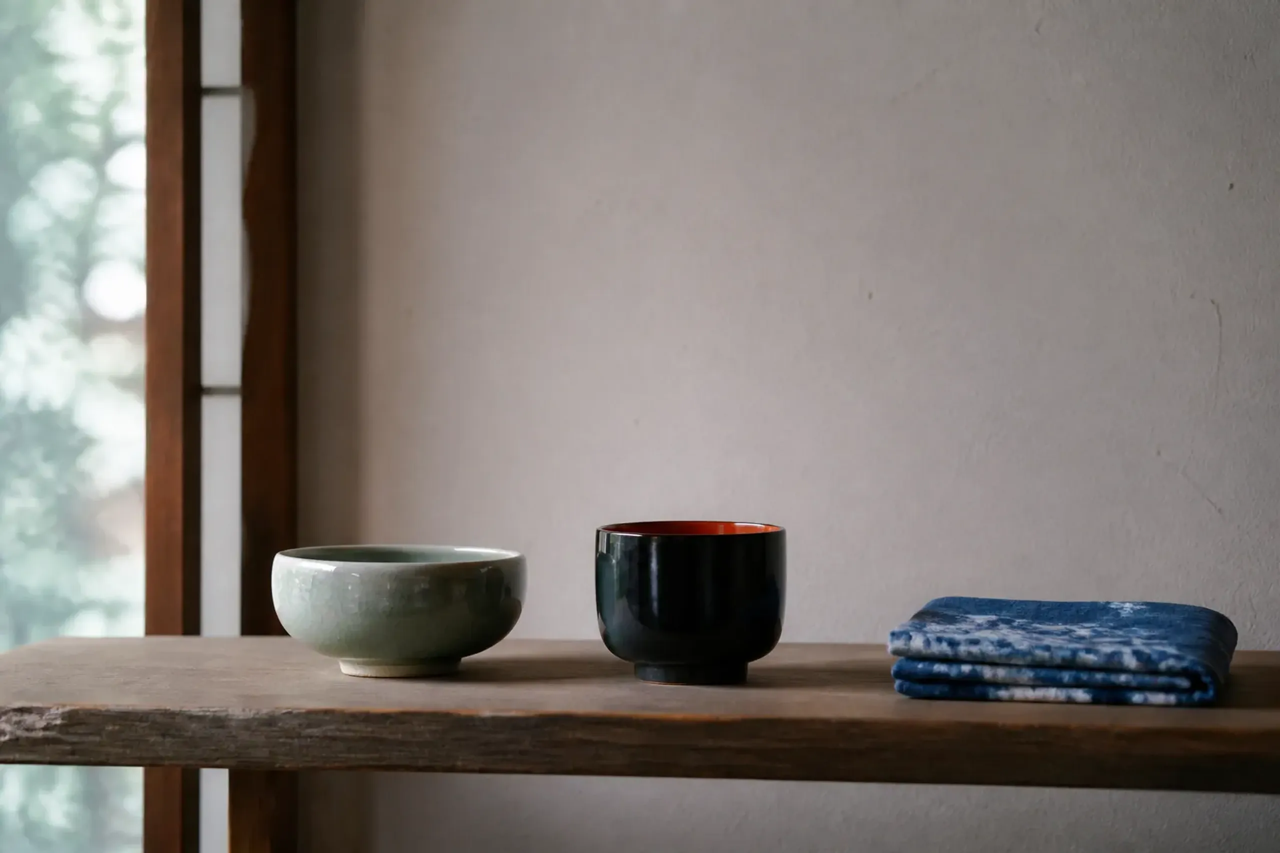 Finished Japanese ceramic, lacquer, and indigo textile objects on a plain wooden shelf