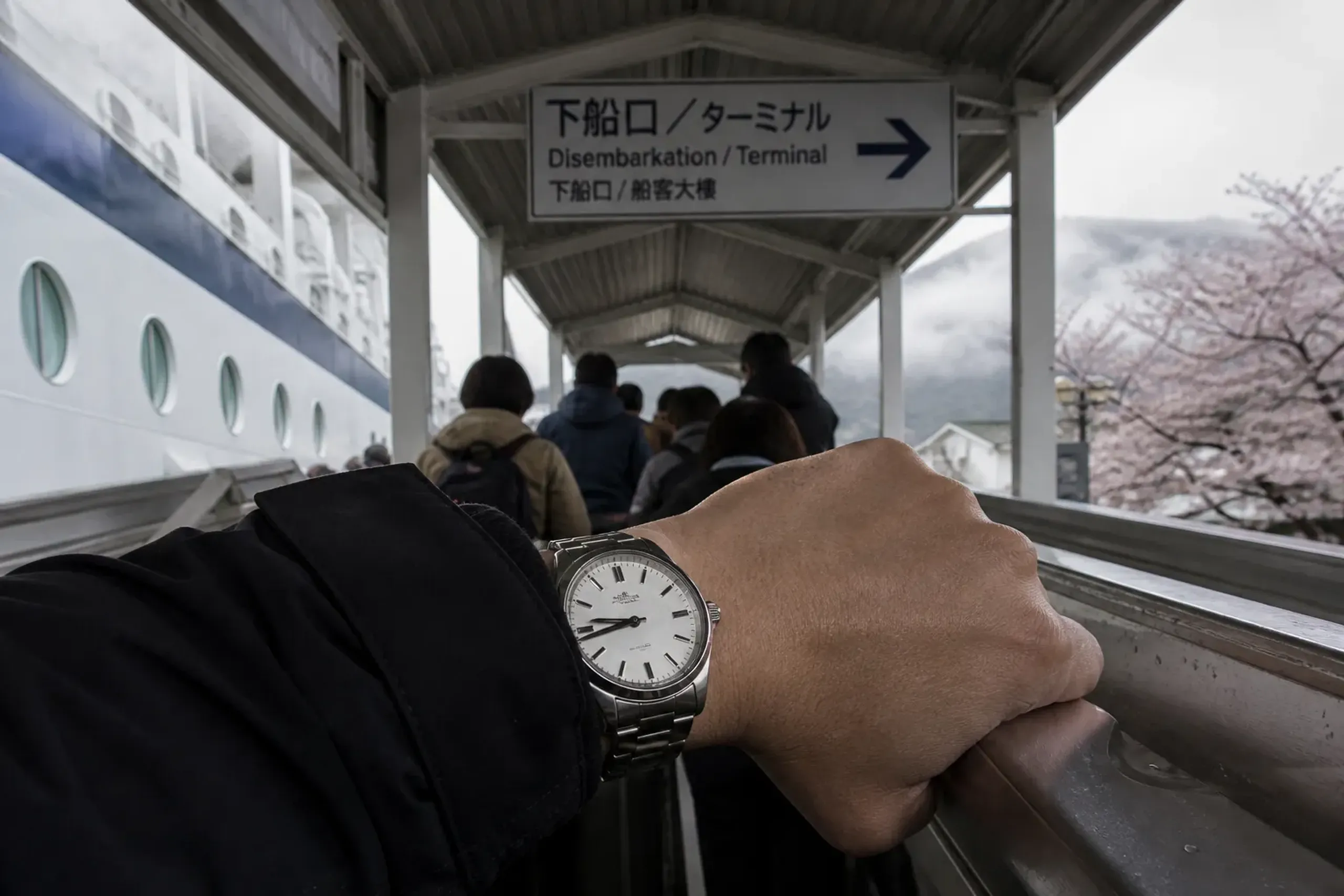 Cruise passengers disembarking at a Japan port with terminal signage and a visible watch