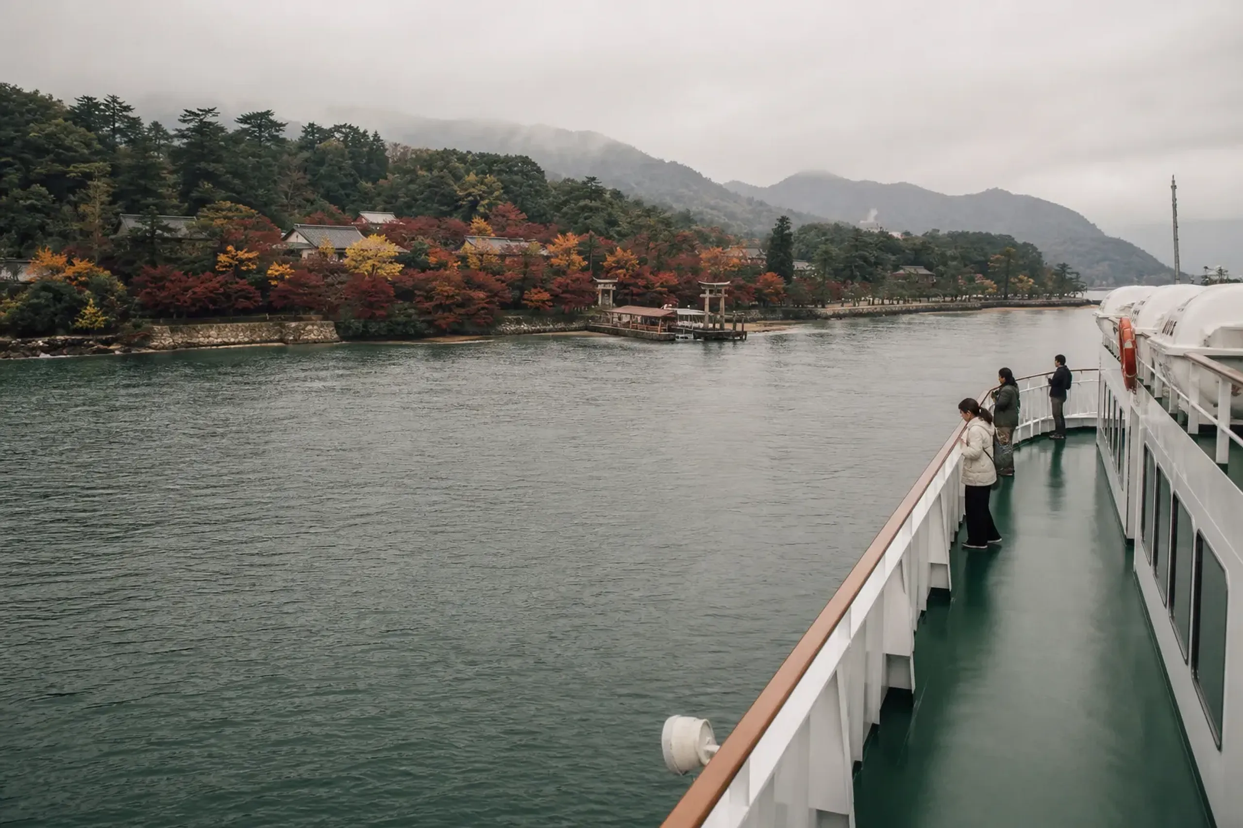 Ferry crossing to Miyajima with passengers on deck and shoreline in the distance
