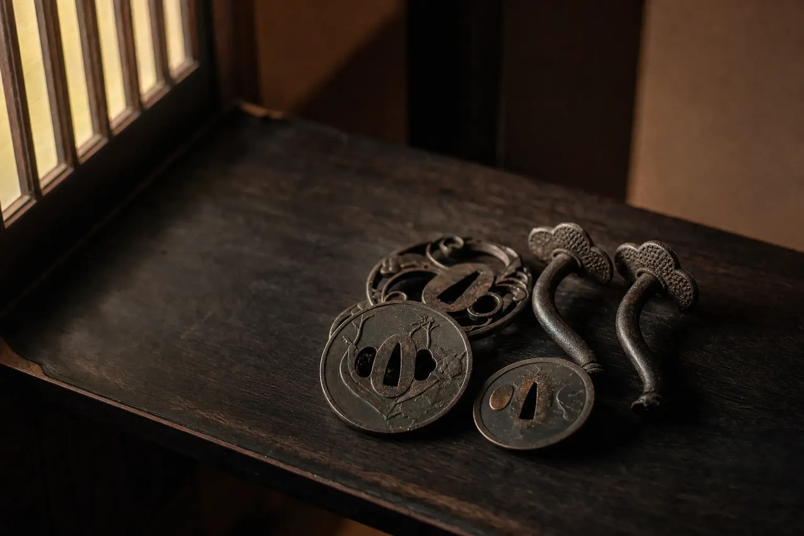 antique sword fittings and cast-metal sliding-door pulls displayed on a dark wooden shelf, remnants of Sumiya's foundry origins
