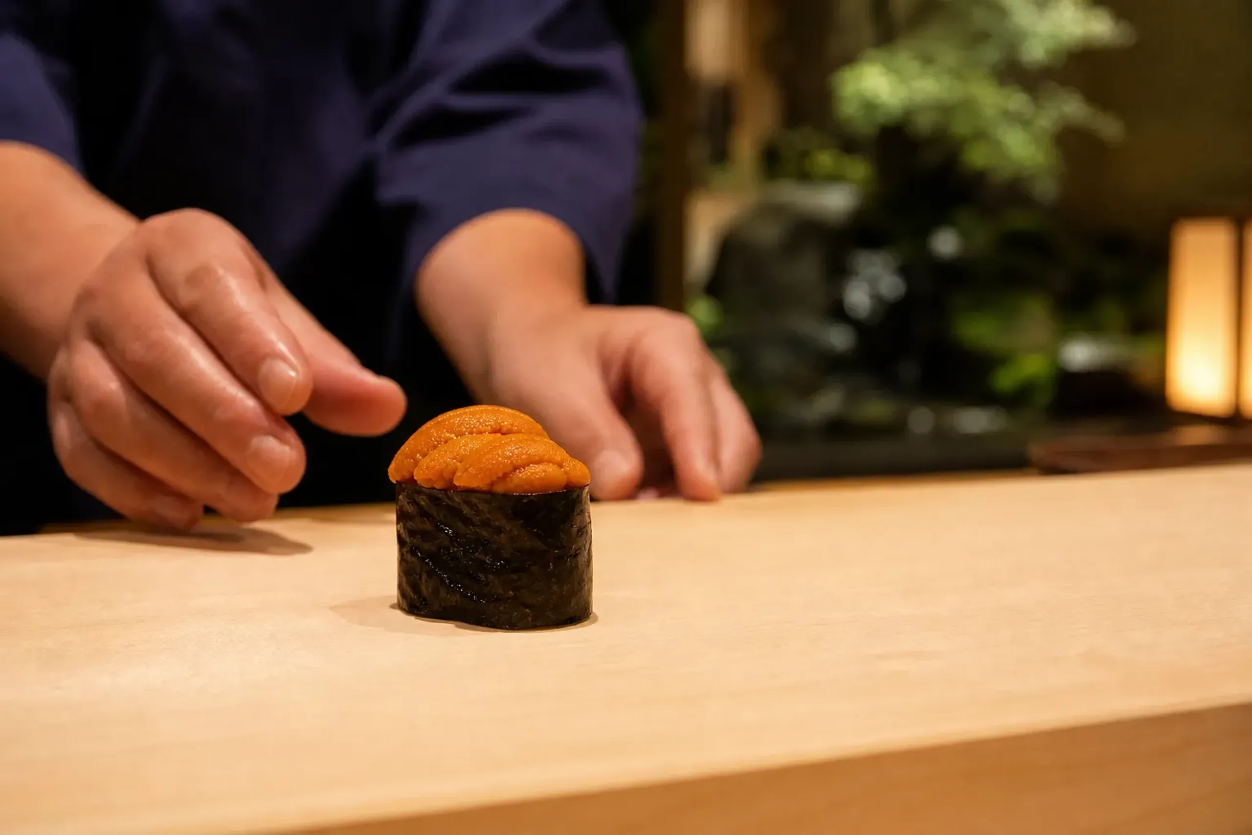 Sushi chef serving uni gunkan sushi at an intimate Japanese counter
