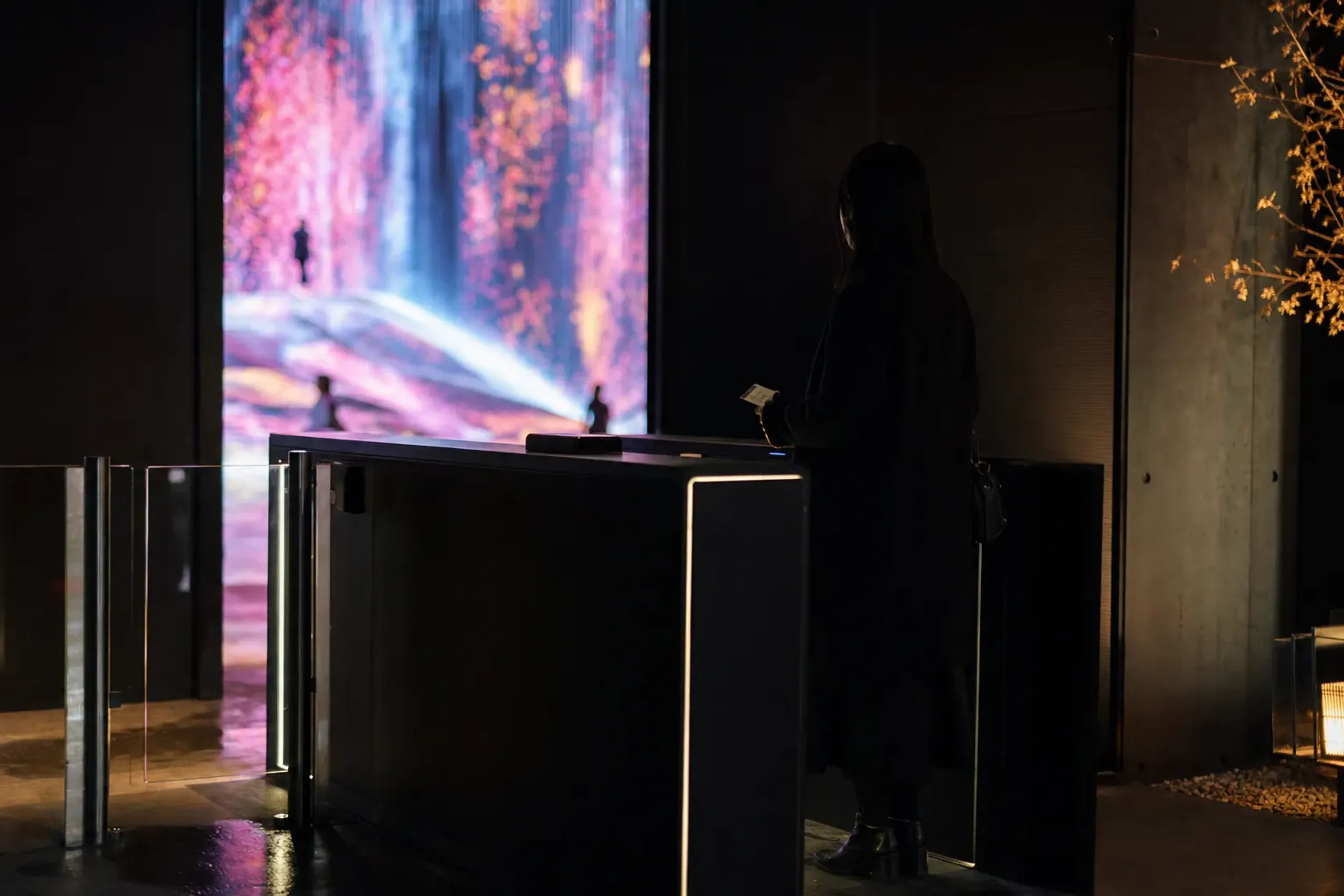 A timed-entry ticket gate at teamLab Borderless, Azabudai Hills, glowing installations visible beyond the entrance