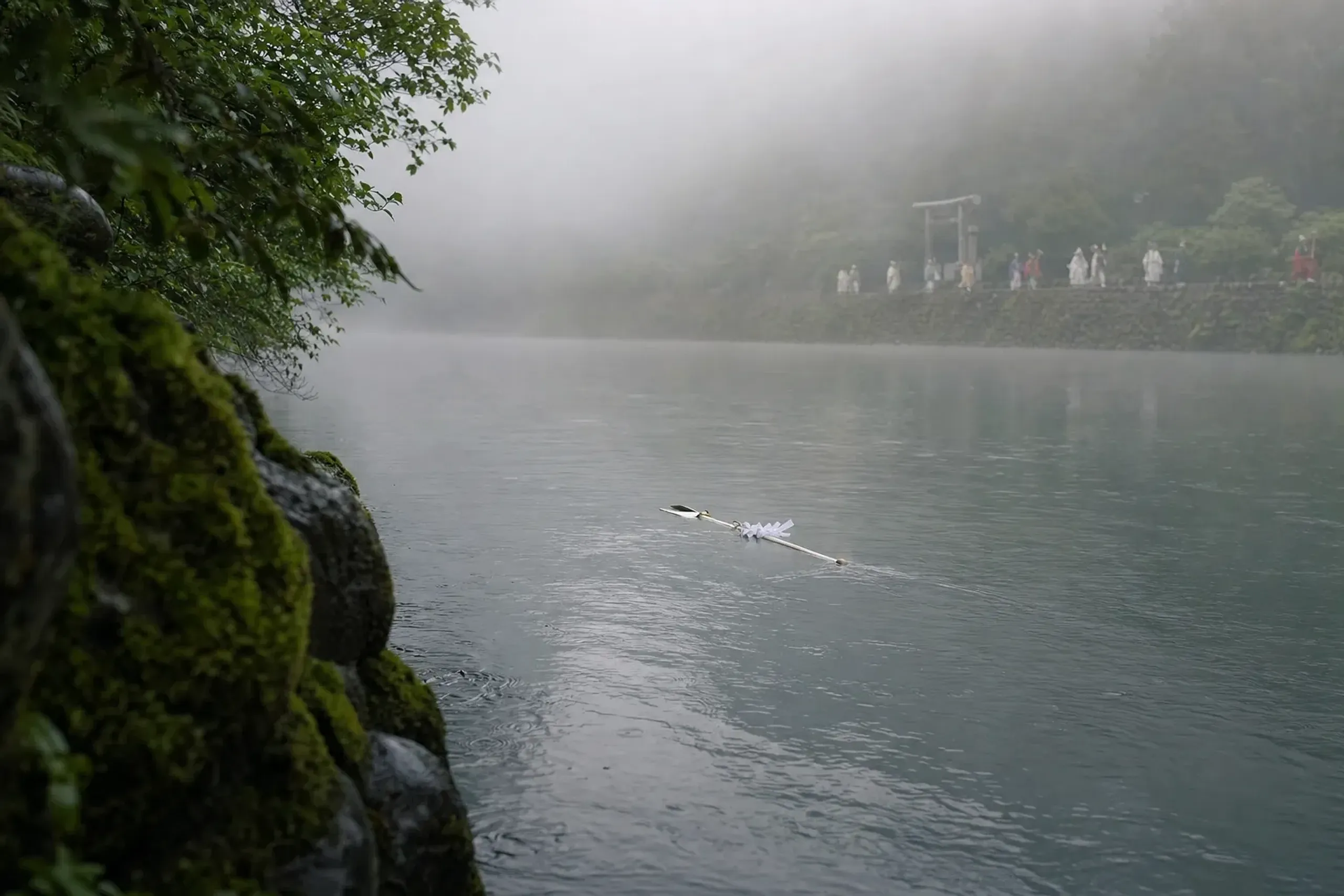 The white-robed released halberd drifting downstream on the Ōkawa River, trailed at a distance by shrine attendants following its path to mark the year's sacred ground