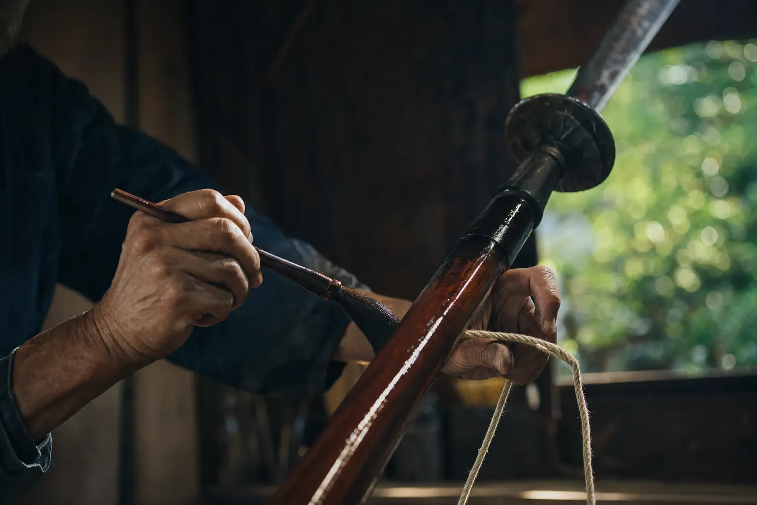 A lacquer master's workshop hands applying lacquer and sacred binding to a festival hoko halberd in an Osaka shokunin studio