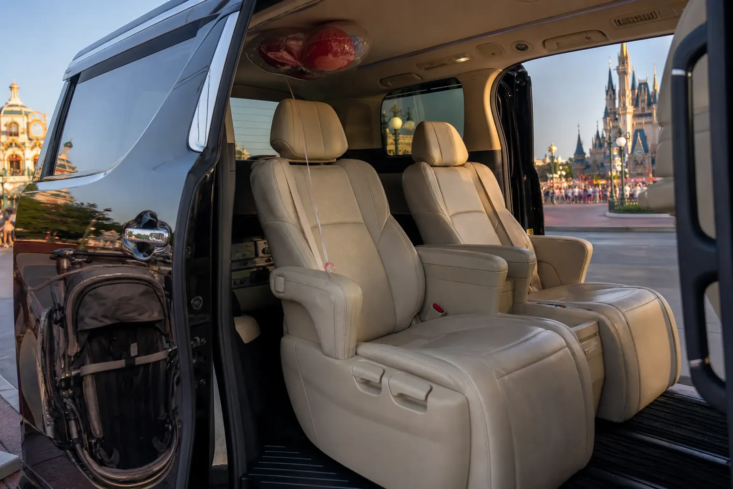 Interior of a black luxury minivan with cream leather seats and a stowed stroller