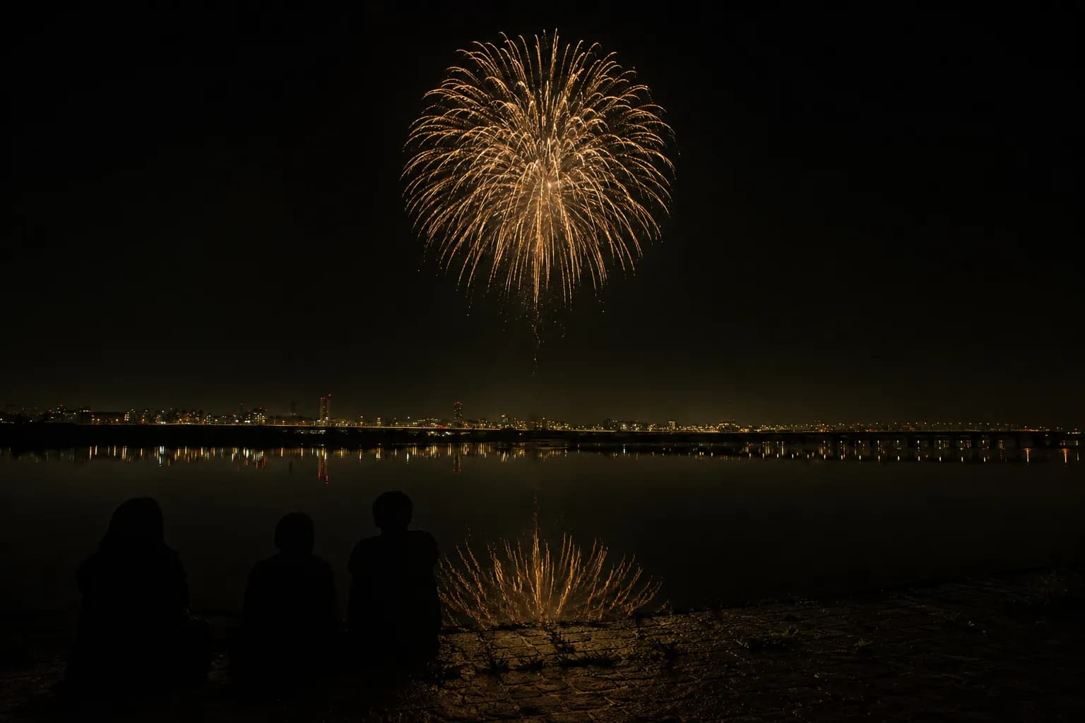 Japanese fireworks bursting above a river at night with silhouetted spectators