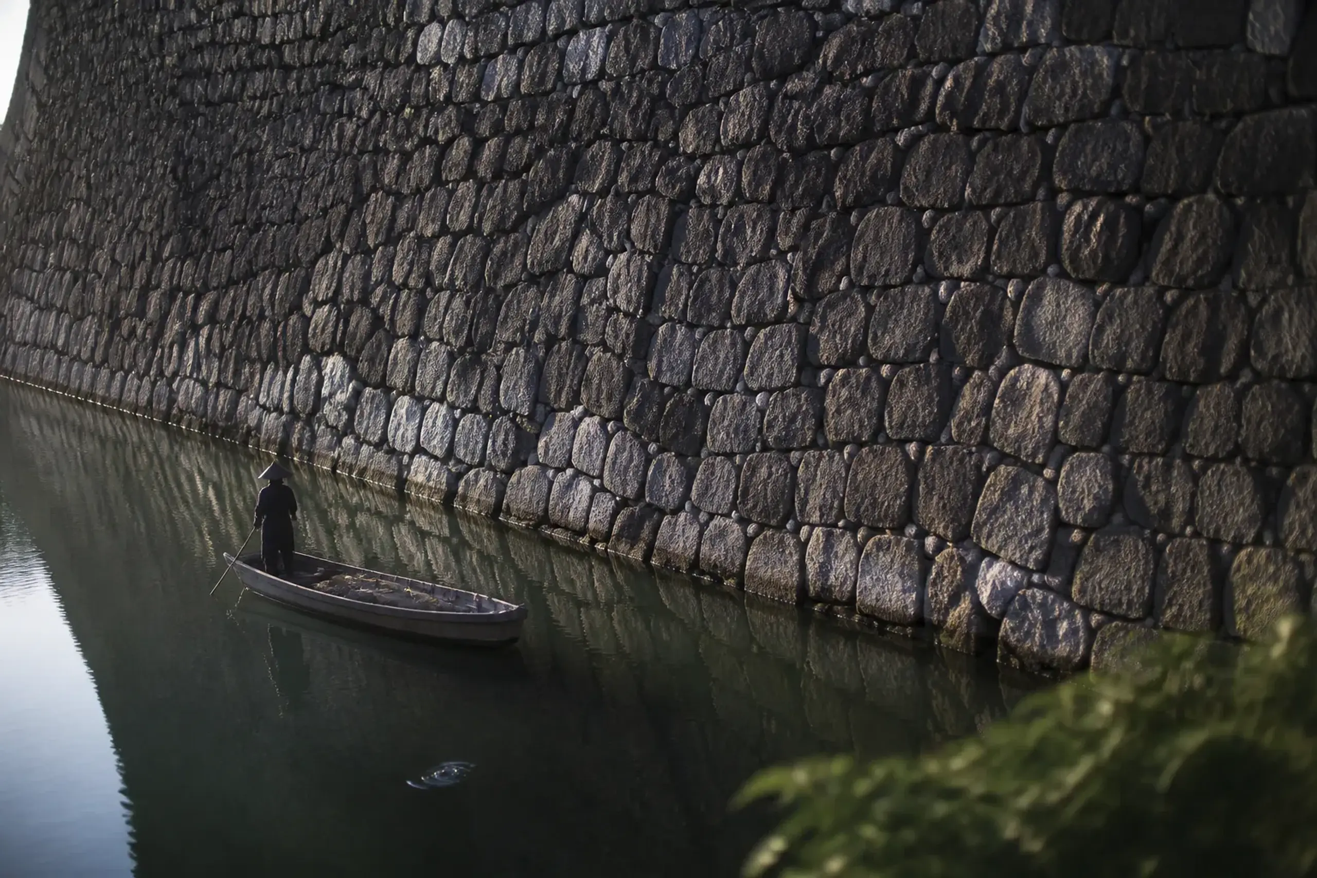 The small wooden boat on the tidal moat of Takamatsu Castle, drifting beneath the towering stone walls at water level