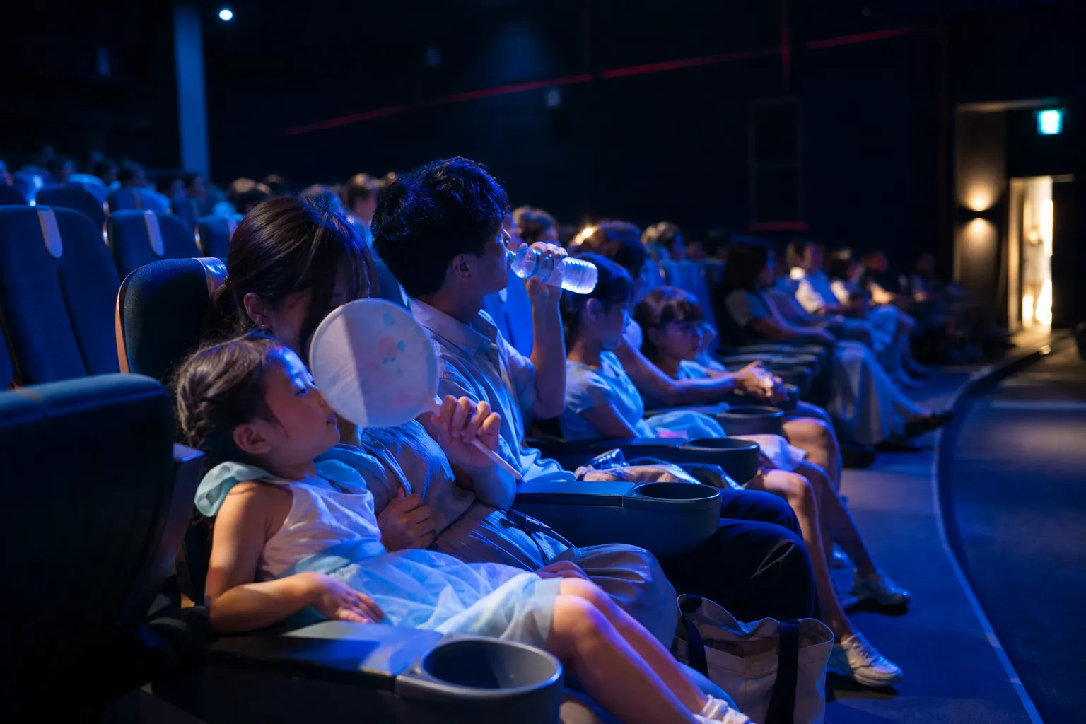 Families resting inside a cool indoor theme park theater during the hottest afternoon hours