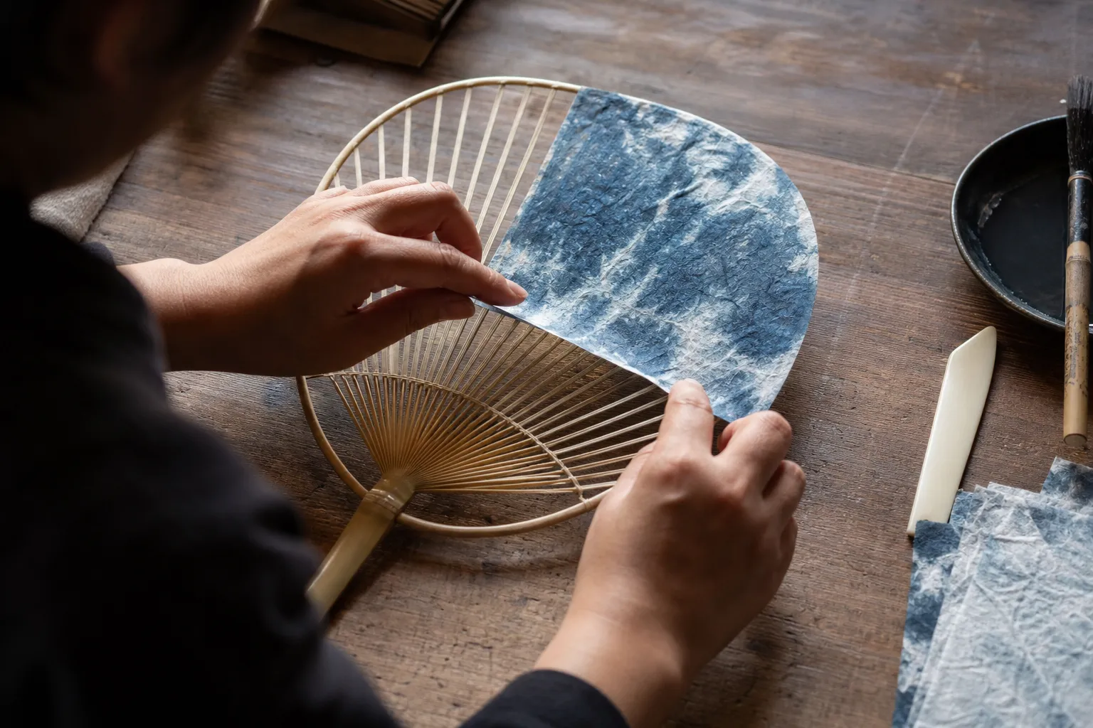 Visitor pasting washi paper onto a bamboo fan frame at a Marugame uchiwa workshop