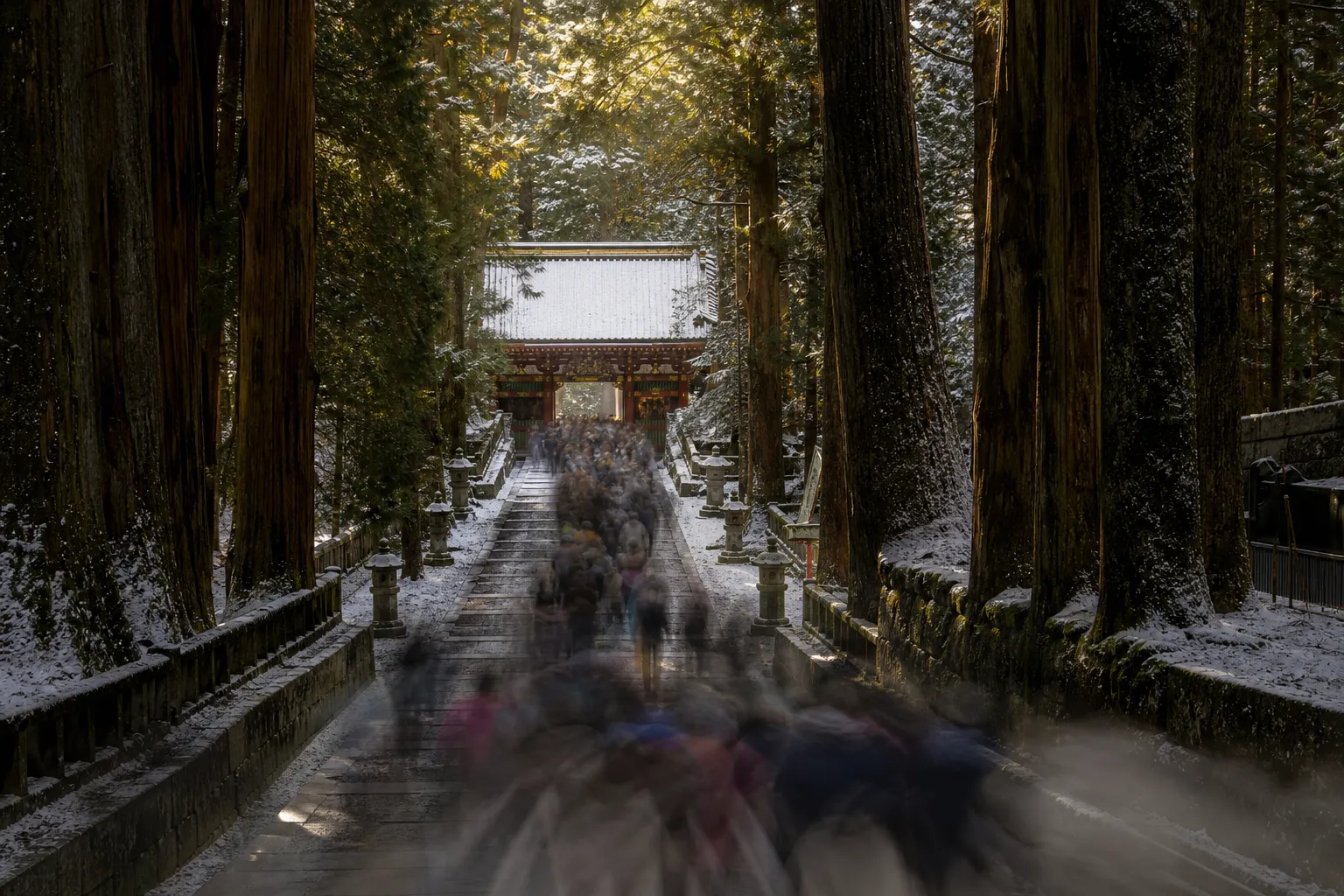 The crowded cedar-lined stone approach leading to the ornate entrance gate of Nikko Toshogu shrine during peak visiting hours, thick with a slow-moving flow of tour groups