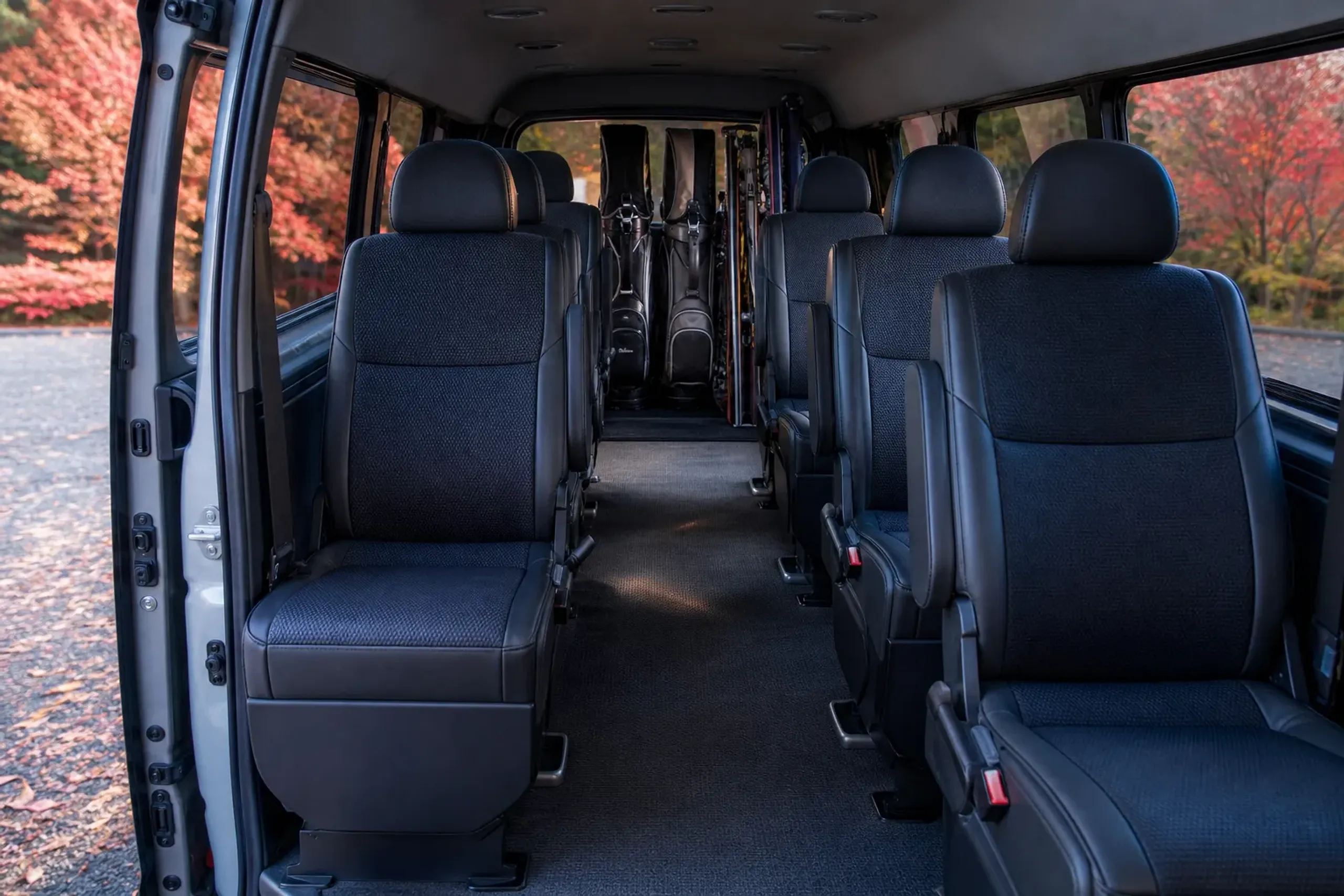 The spacious interior of a Toyota HiAce with rows of empty passenger seats and golf bags and ski gear loaded in the rear cargo area
