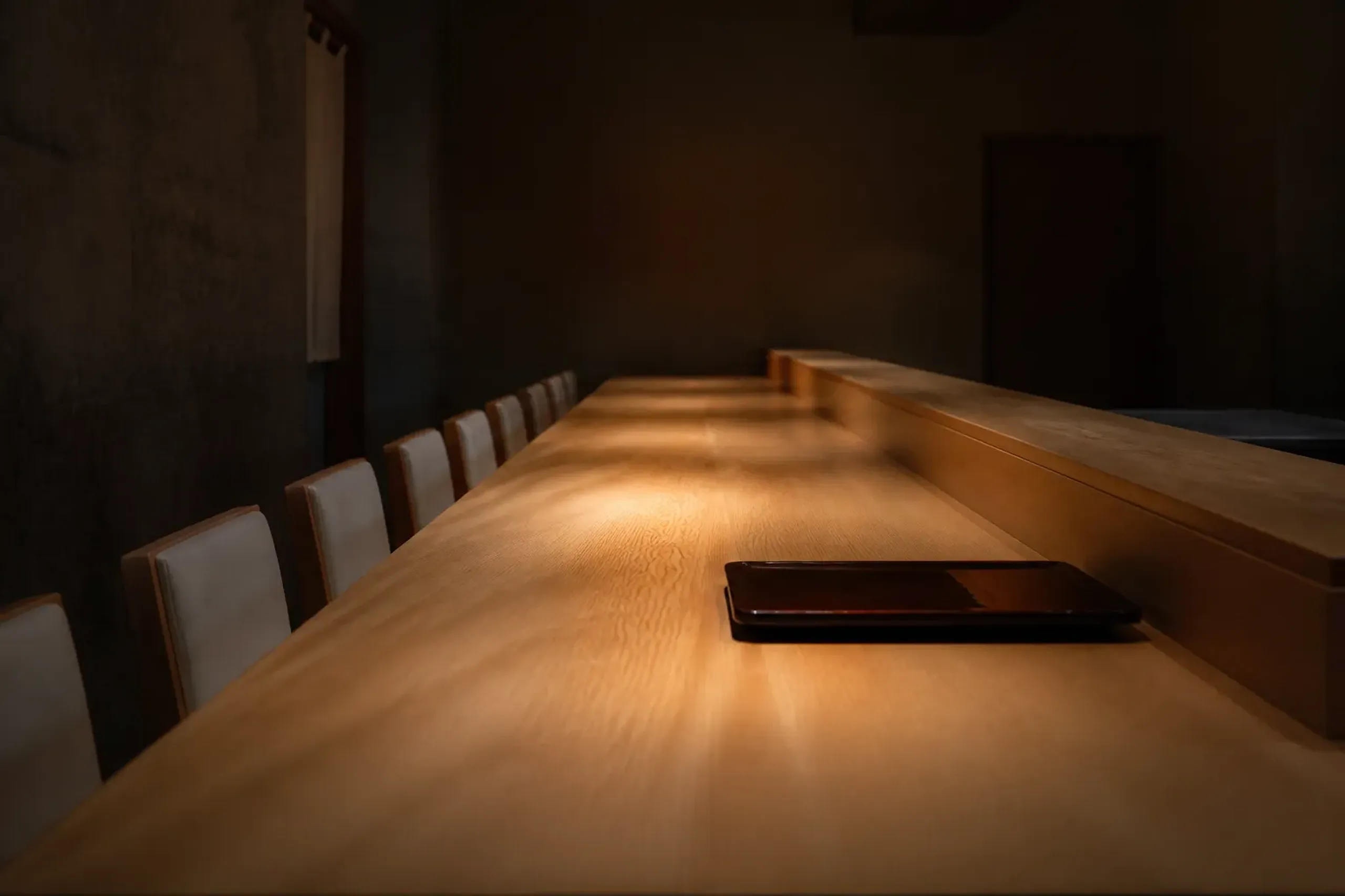An eight-seat wooden hinoki counter in a Kyoto establishment, worn smooth and polished from generations of use, standing empty and immaculate under warm low lighting
