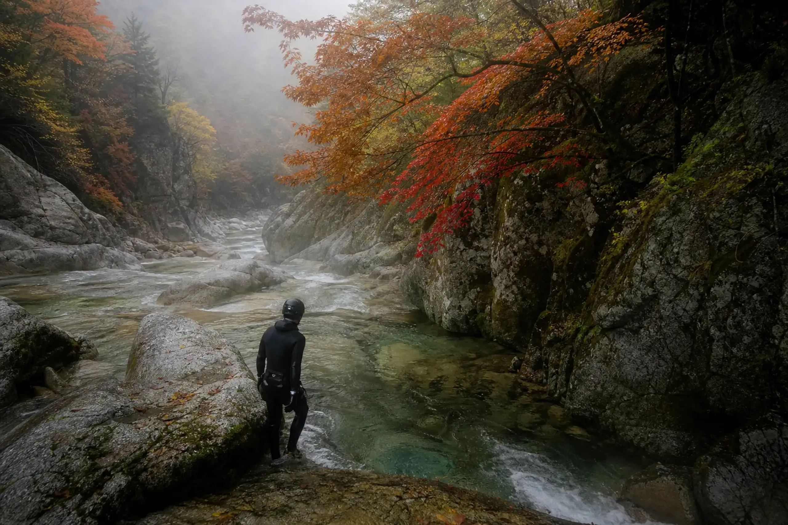 Canyoning participant stepping into a narrow granite gorge with clear running water in the Japanese Alps