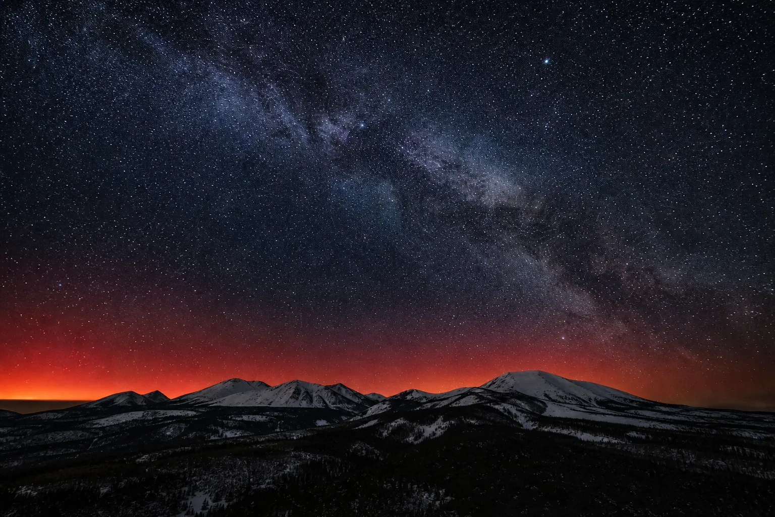 Starry night sky with a faint red aurora-like glow over a dark ridgeline in Hokkaido, Japan