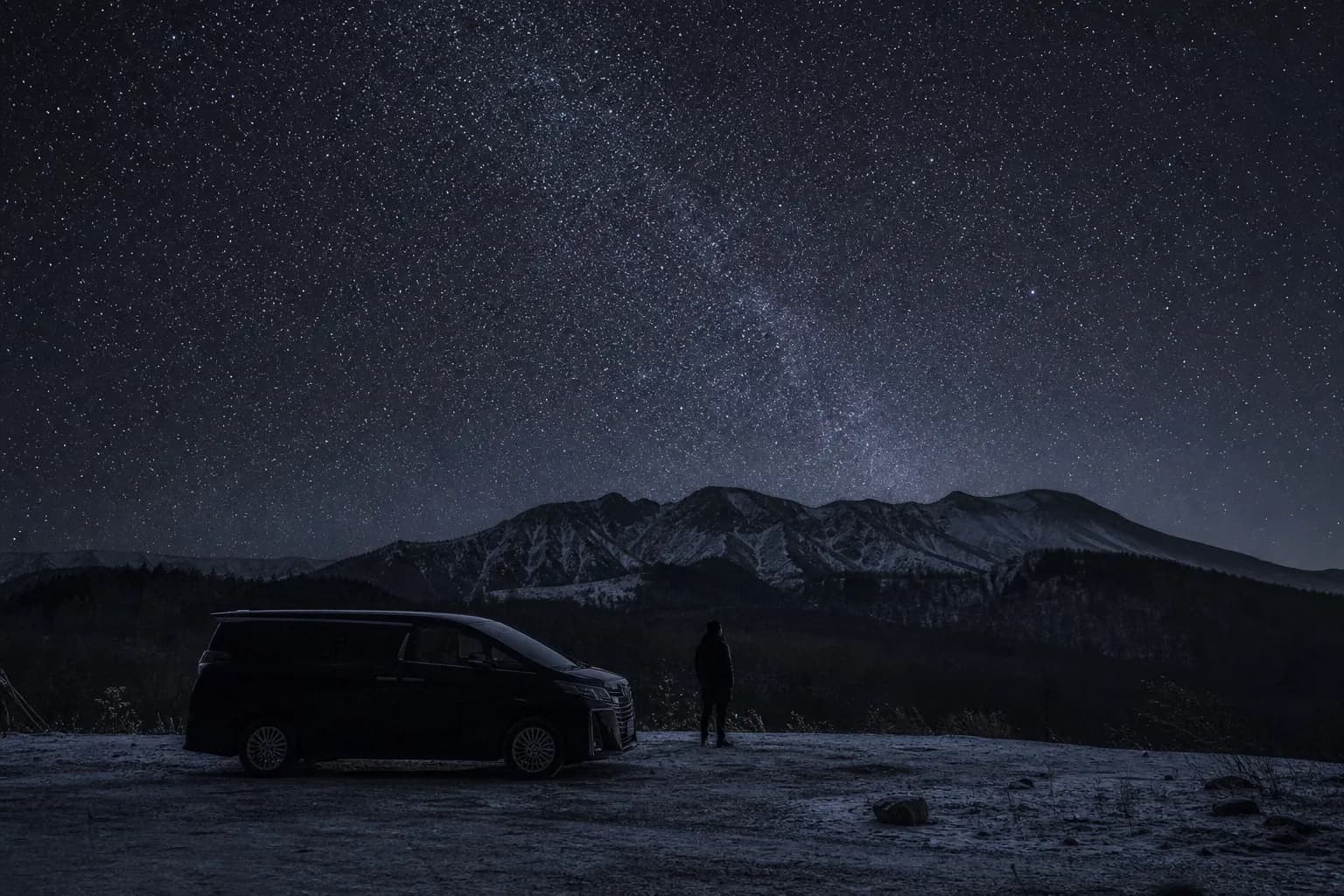 Private vehicle waiting at a dark roadside viewpoint while a traveler looks up at the stars in Hokkaido