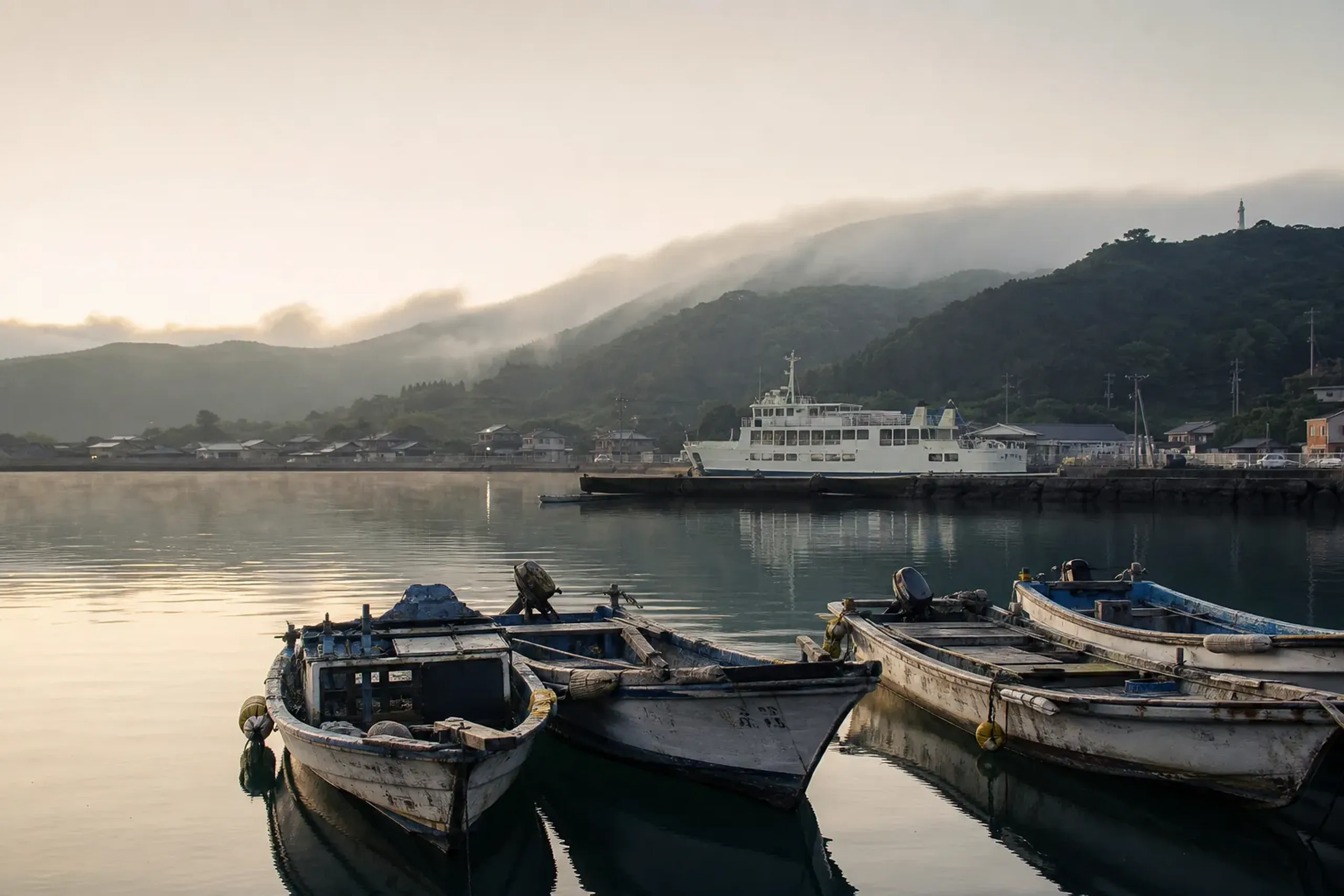 Small harbor on an inhabited Oki Island with fishing boats and a ferry, backed by green hills