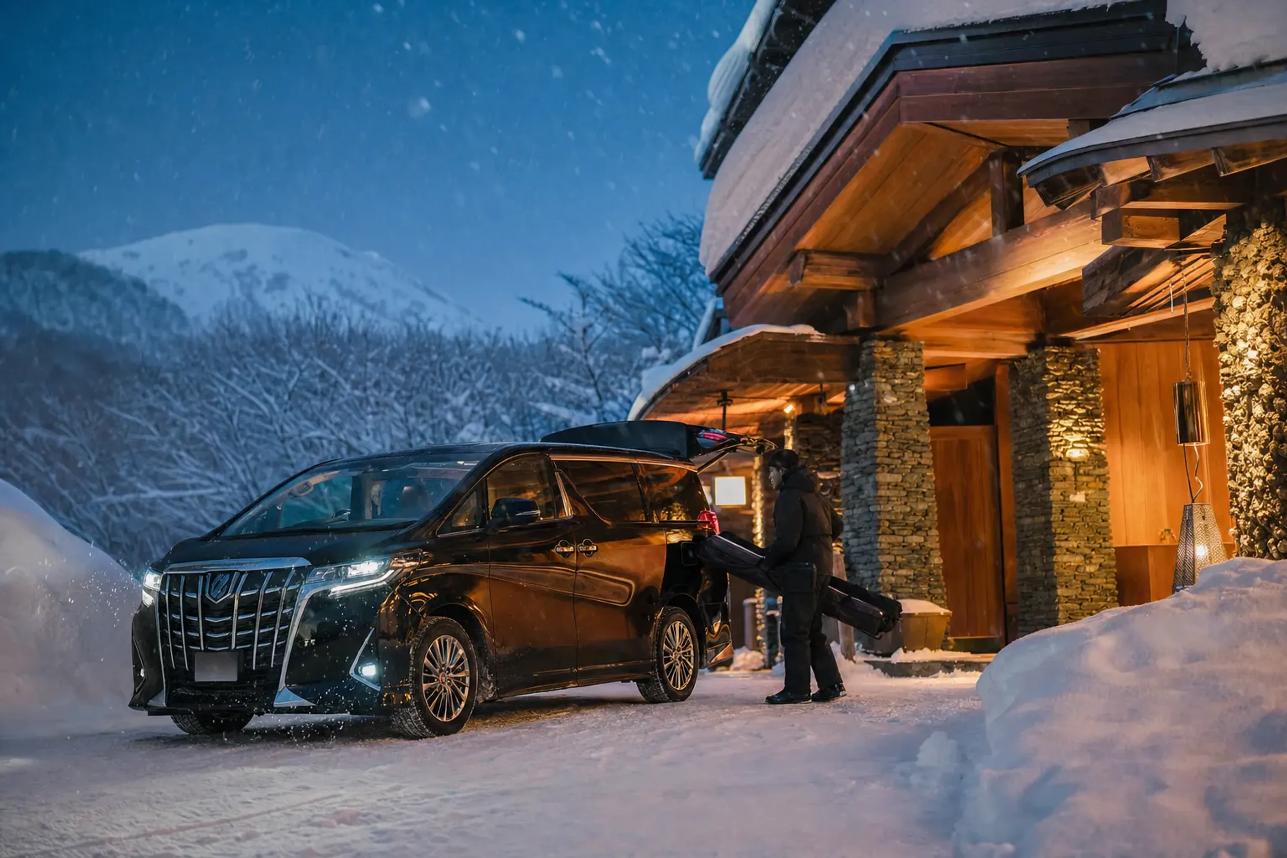 Luxury private transfer vehicle at a snowy Niseko chalet entrance with ski gear