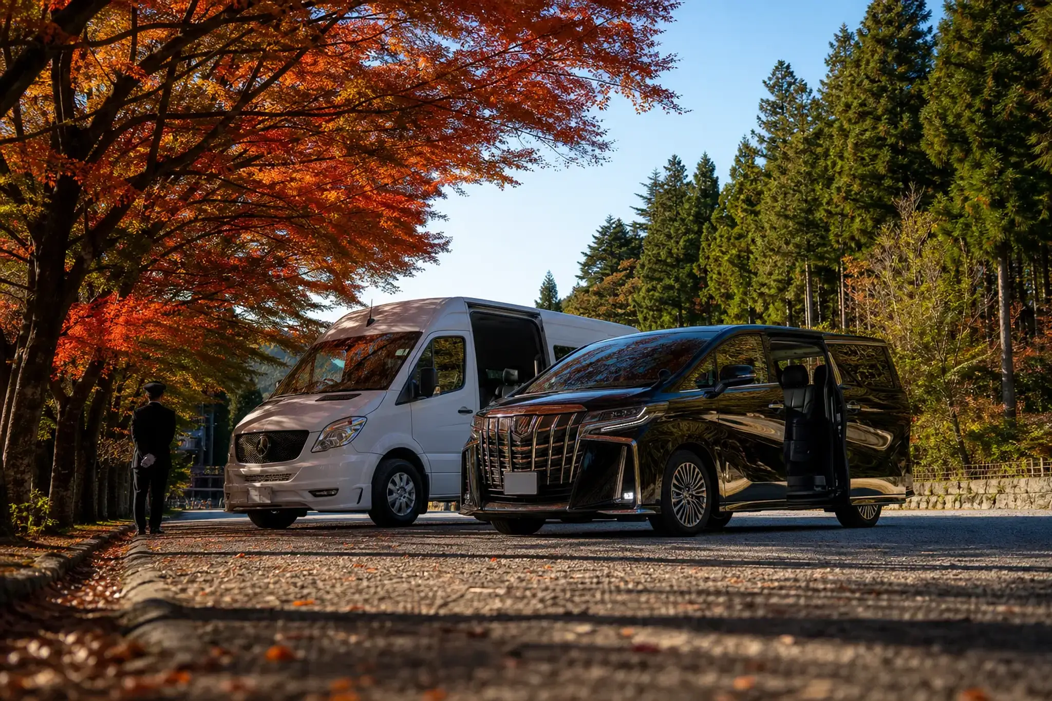 A white Mercedes Sprinter touring van parked beside a black Toyota Alphard on a Japanese roadway