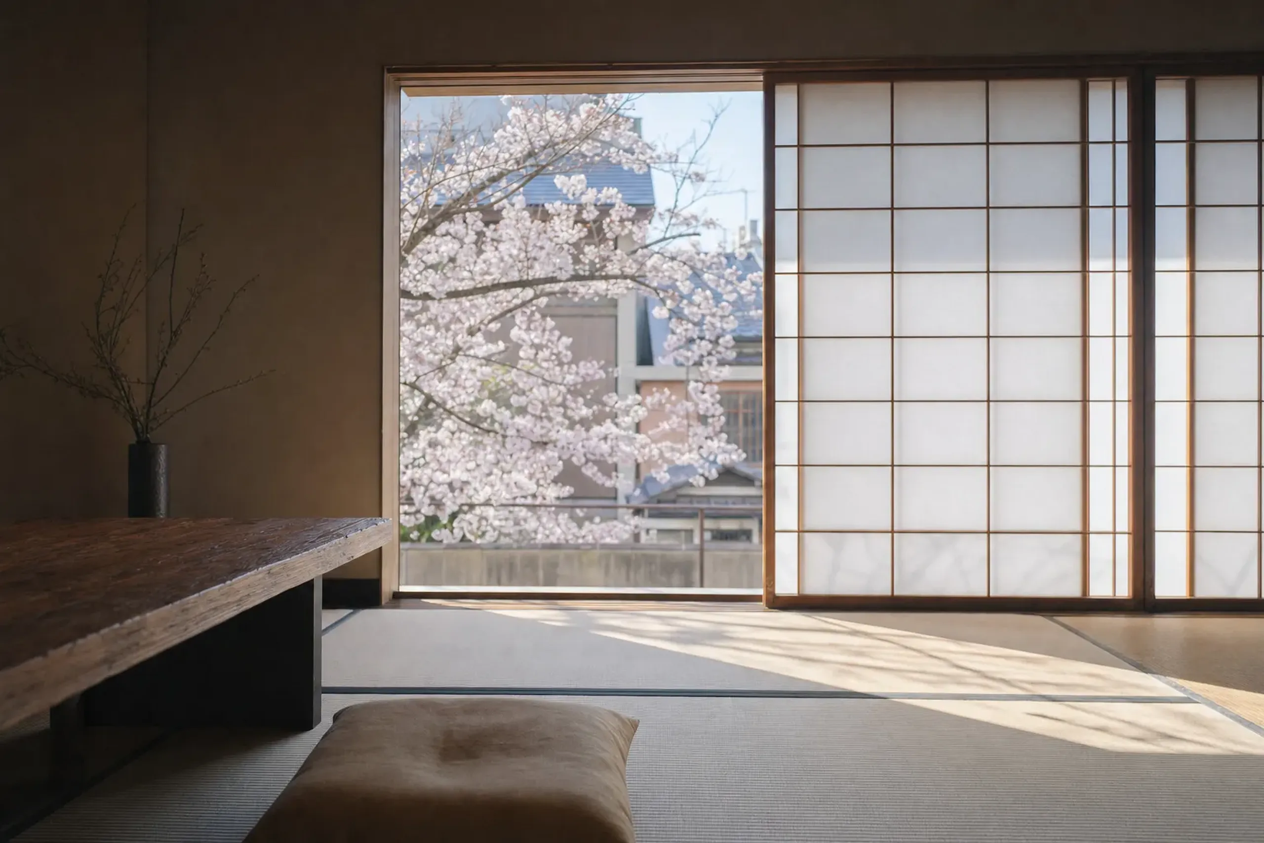 A tatami-floored suite interior at The Shinmonzen with shoji screens filtering soft daylight across muted, tactile surfaces