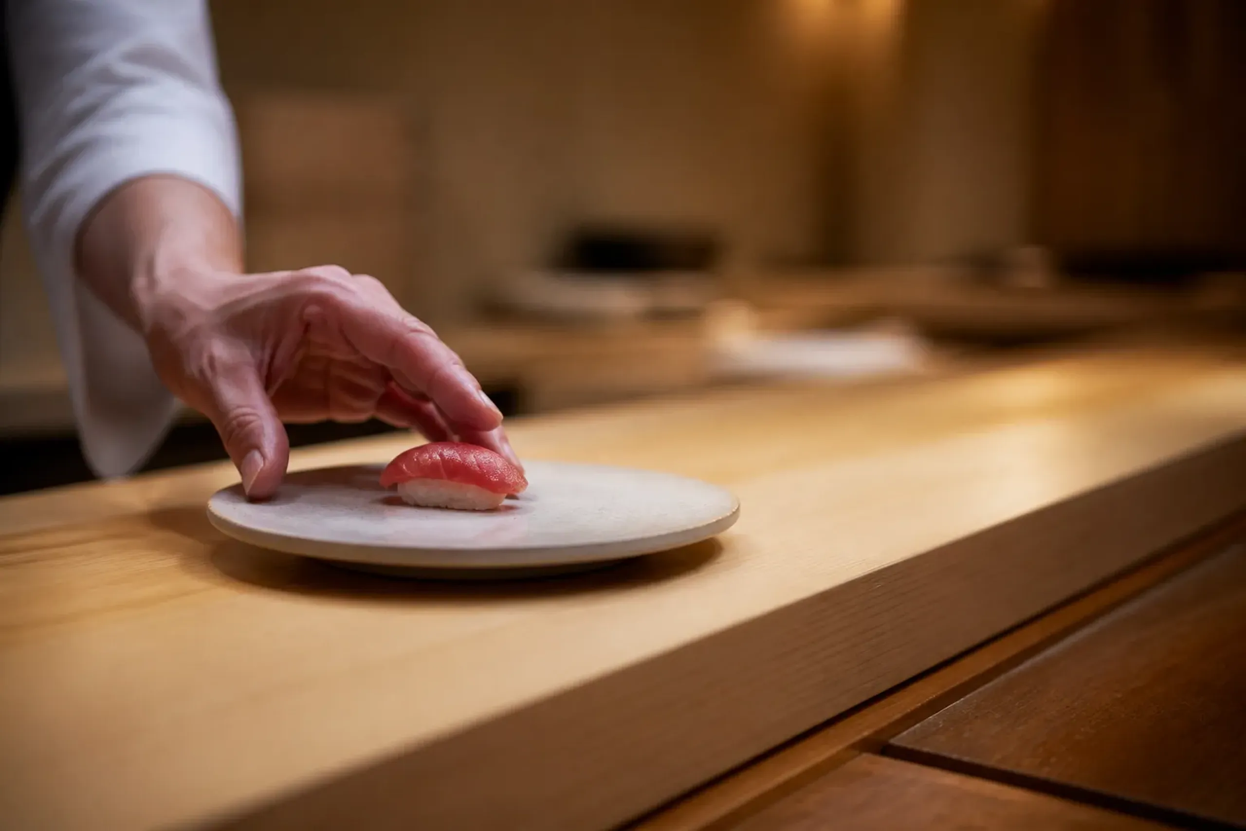 Chef placing nigiri sushi on a plate at a wooden counter in an intimate sushi restaurant