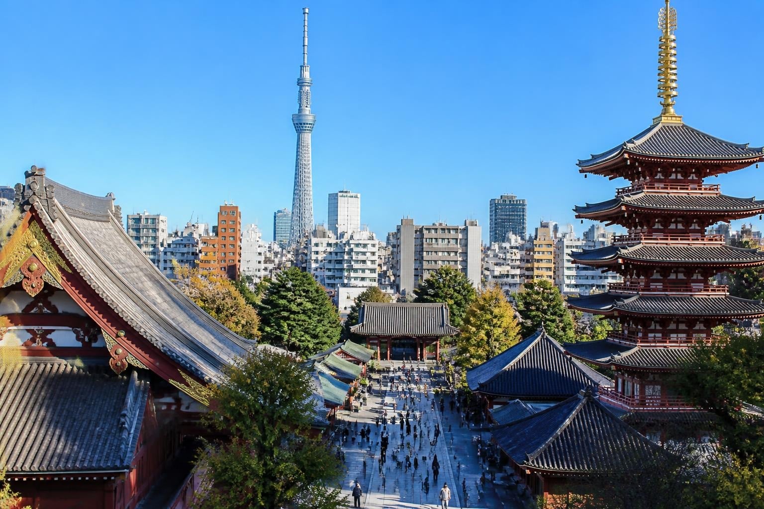 Senso-ji temple complex with a five-story pagoda in the foreground and Tokyo Skytree in the distance on a clear day.