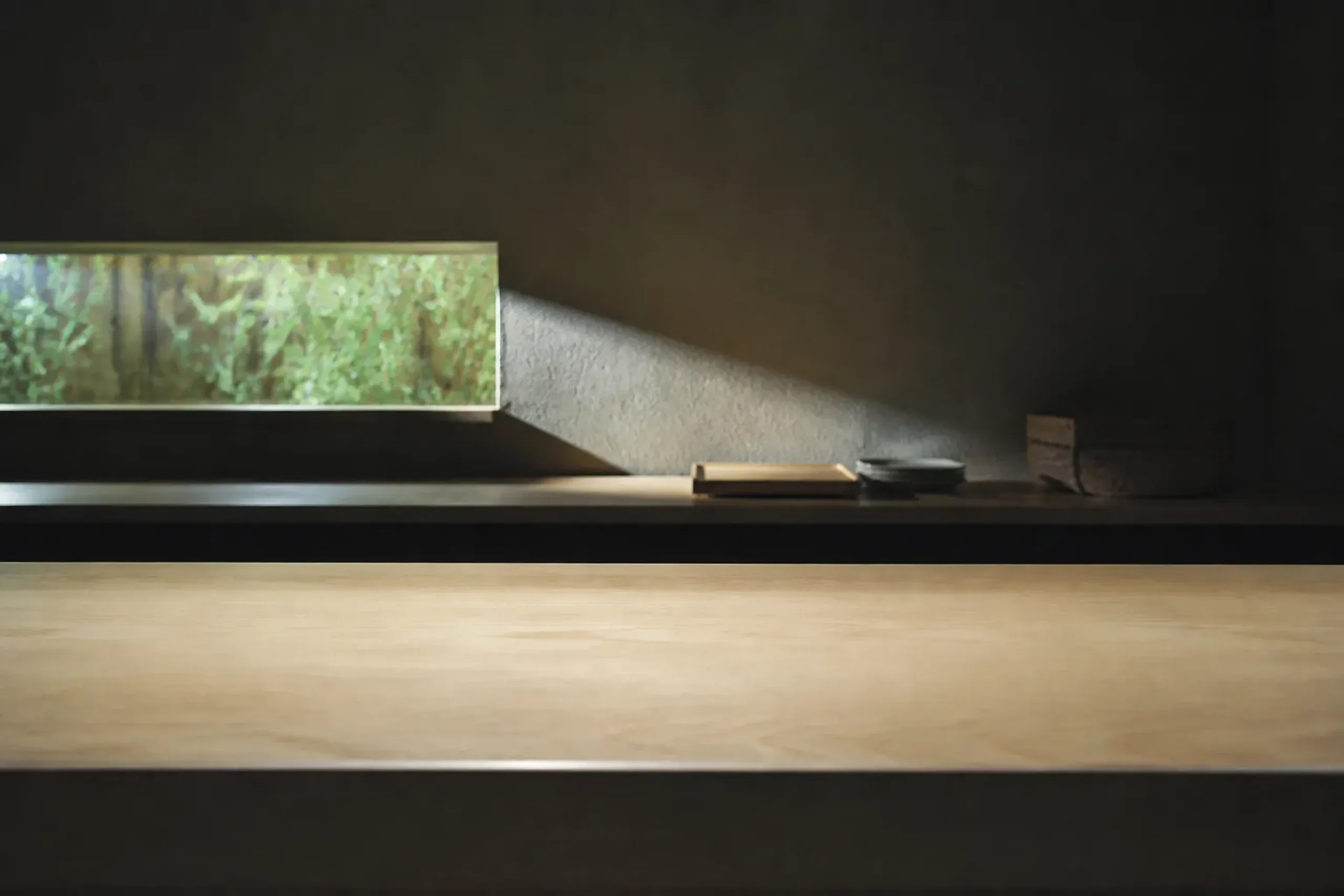 A plain wiped-down Japanese cypress kaiseki counter surface before service, empty and bare, with the chef's station behind it, in a small quiet Kyoto dining room