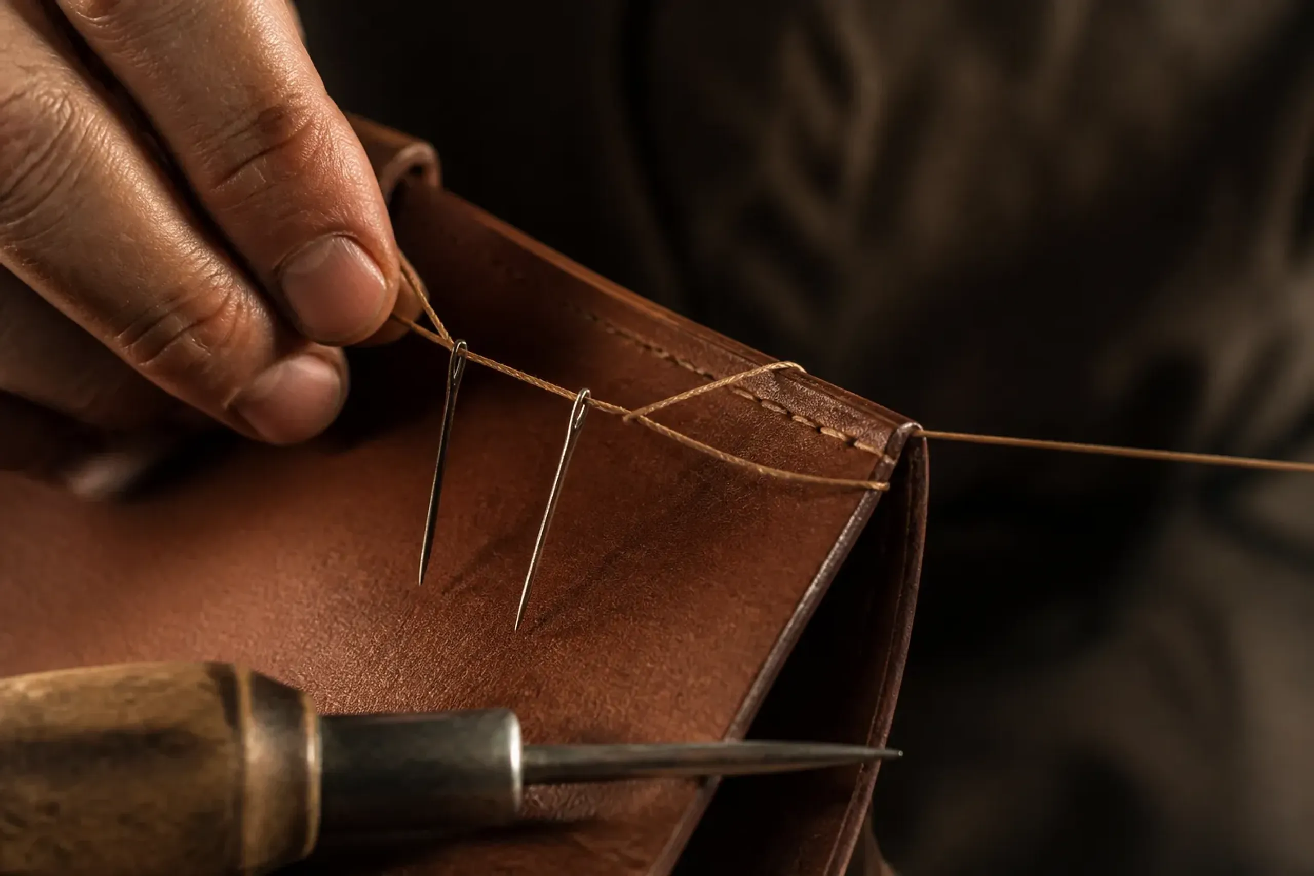 Close-up of hand saddle stitching along a leather briefcase edge with diagonal stitch line